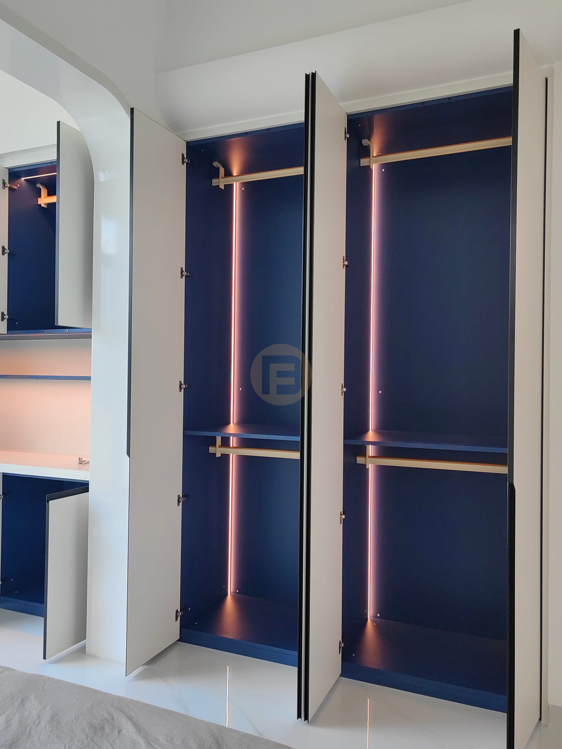 Open wardrobe doors revealing navy interiors with brass rails and vertical LED strips