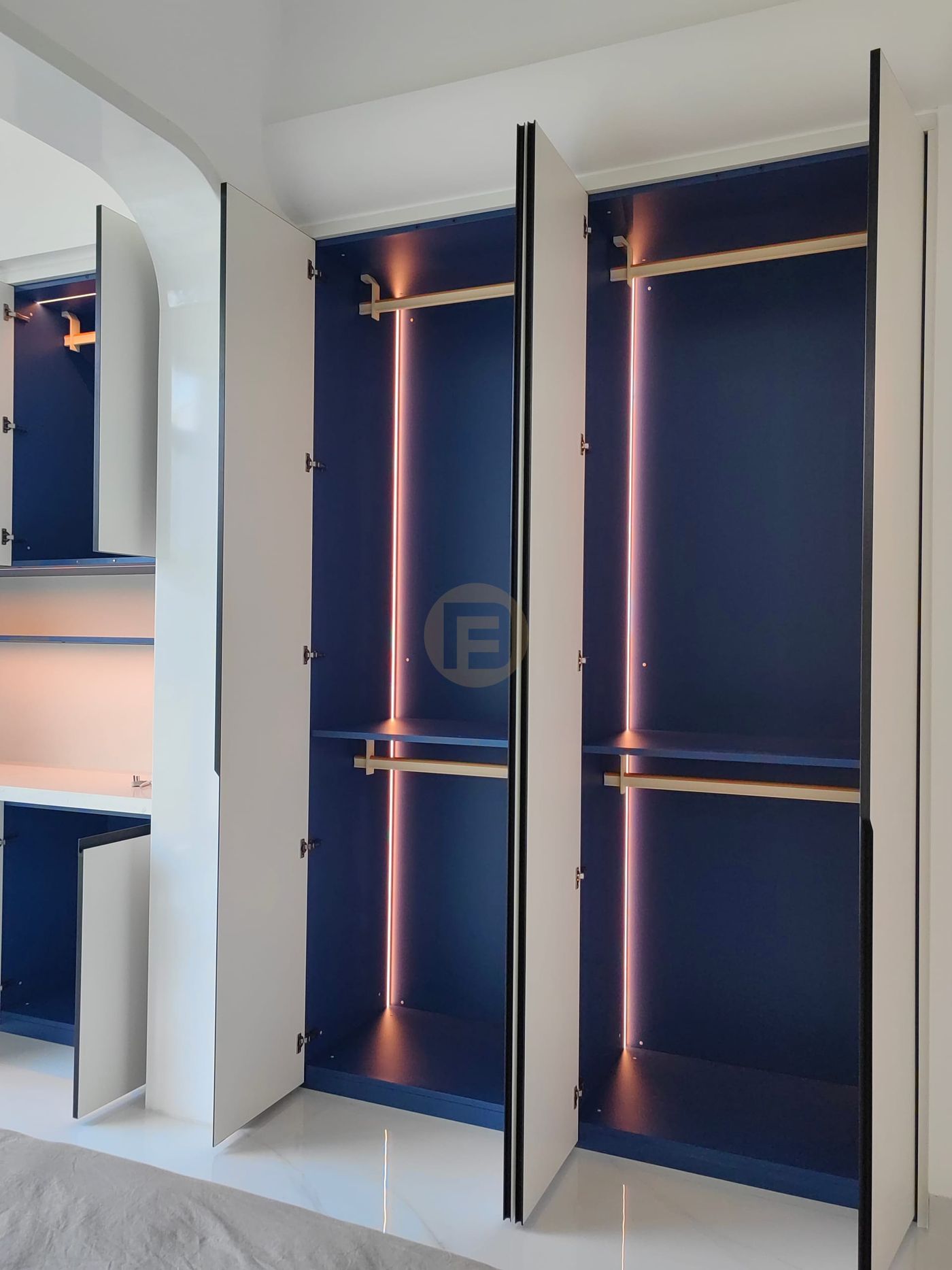 Open wardrobe doors revealing navy interiors with brass rails and vertical LED strips