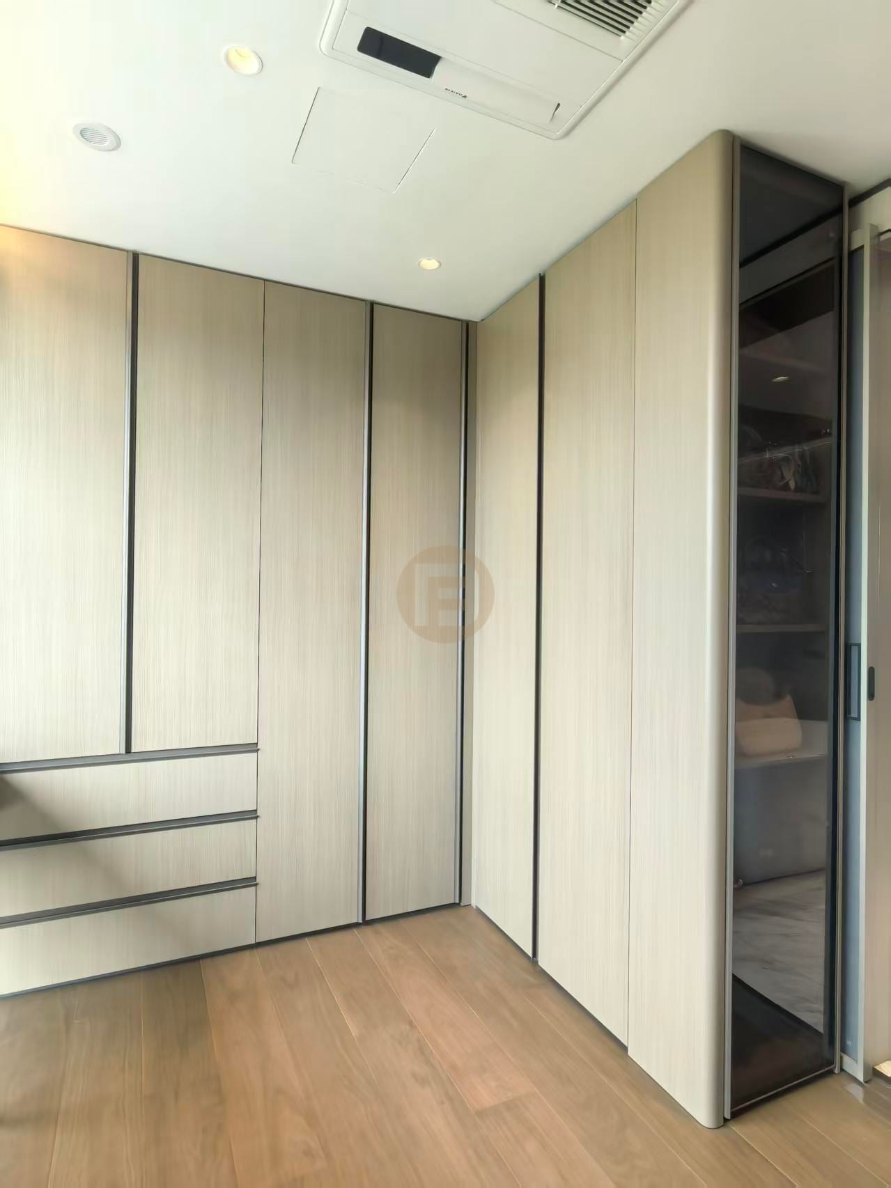 Walk-in closet corner in light greige stainless steel panels with a smoked-glass cabinet door