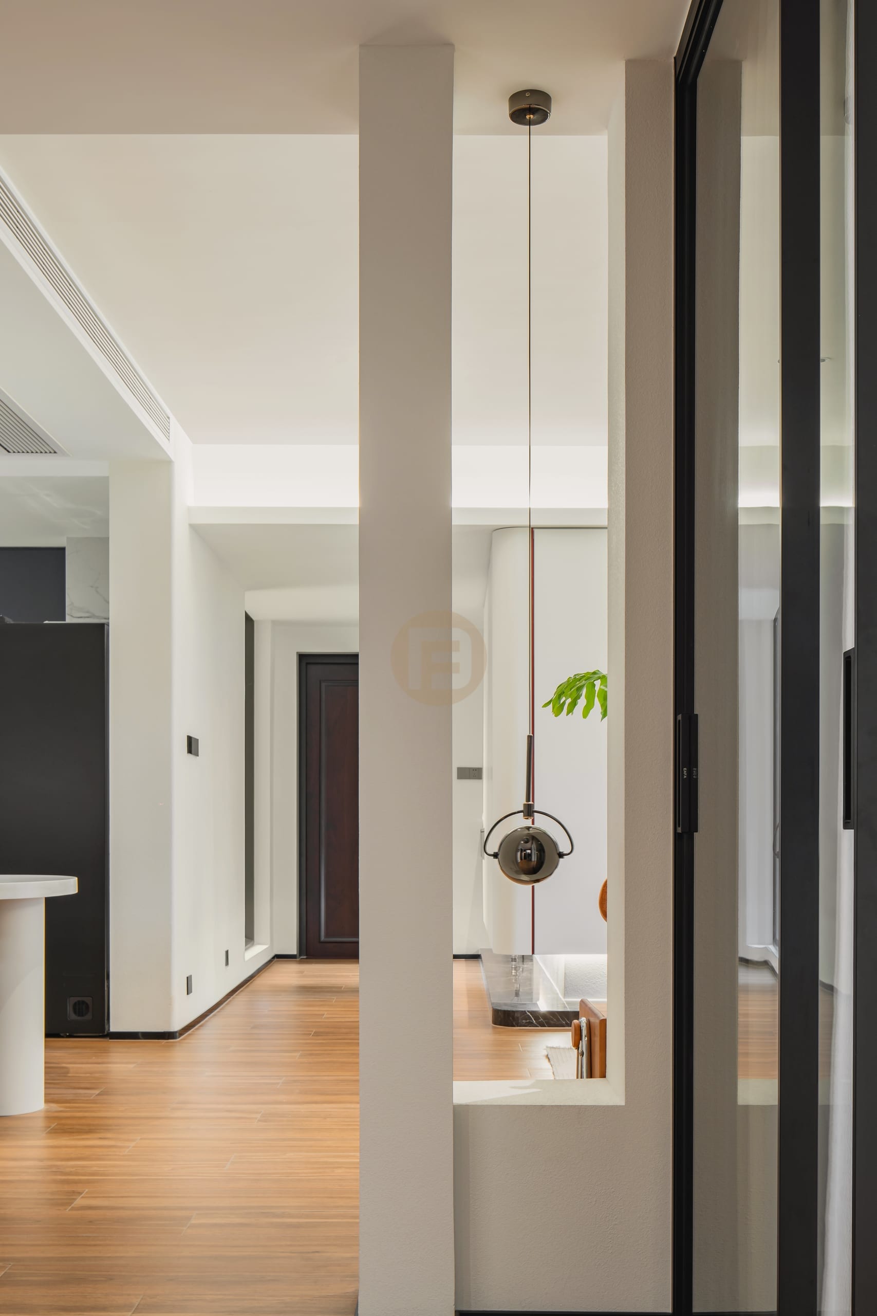 Hallway framed by a white partition and black-framed glass screen with a sculptural pendant light