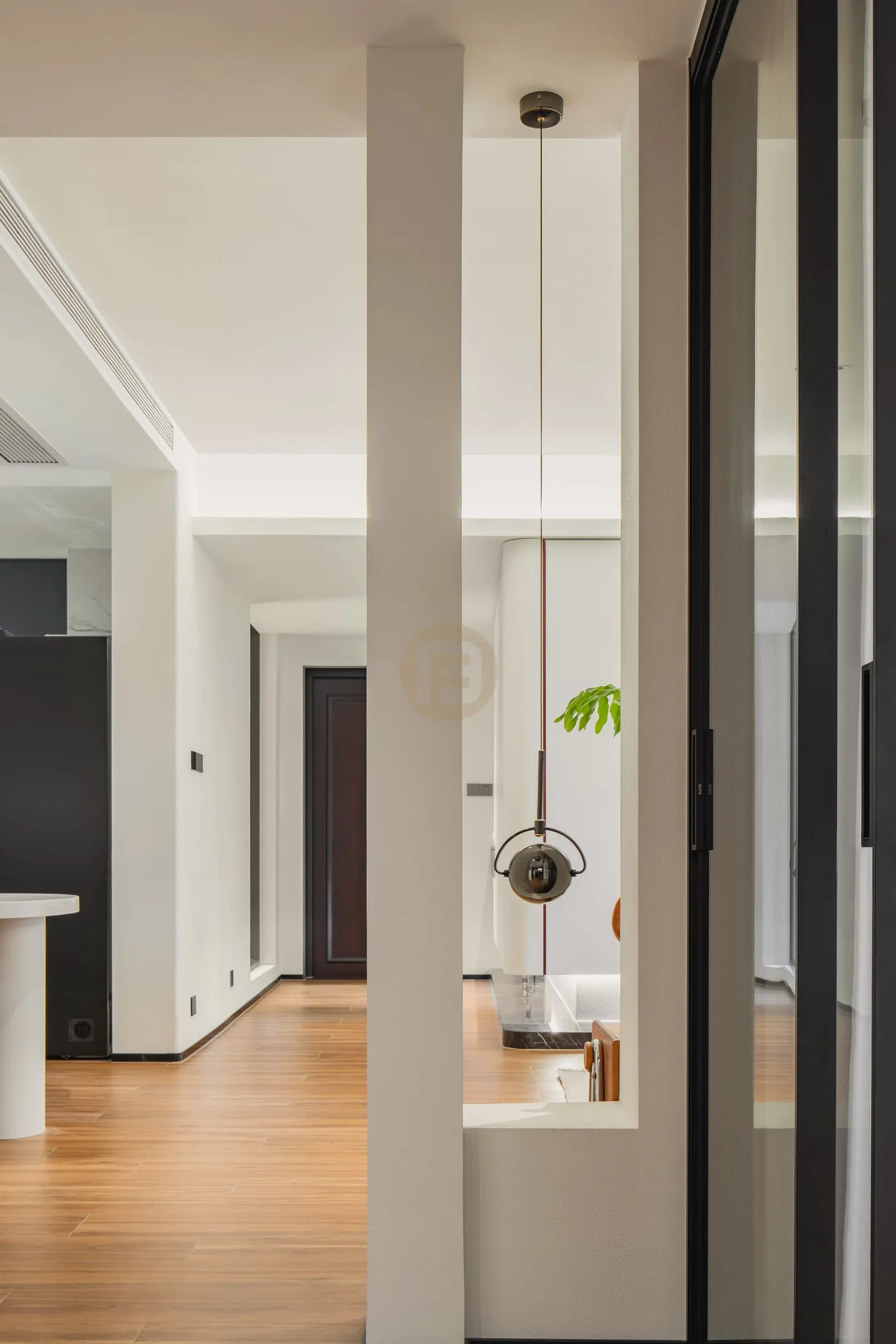 Hallway framed by a white partition and black-framed glass screen with a sculptural pendant light