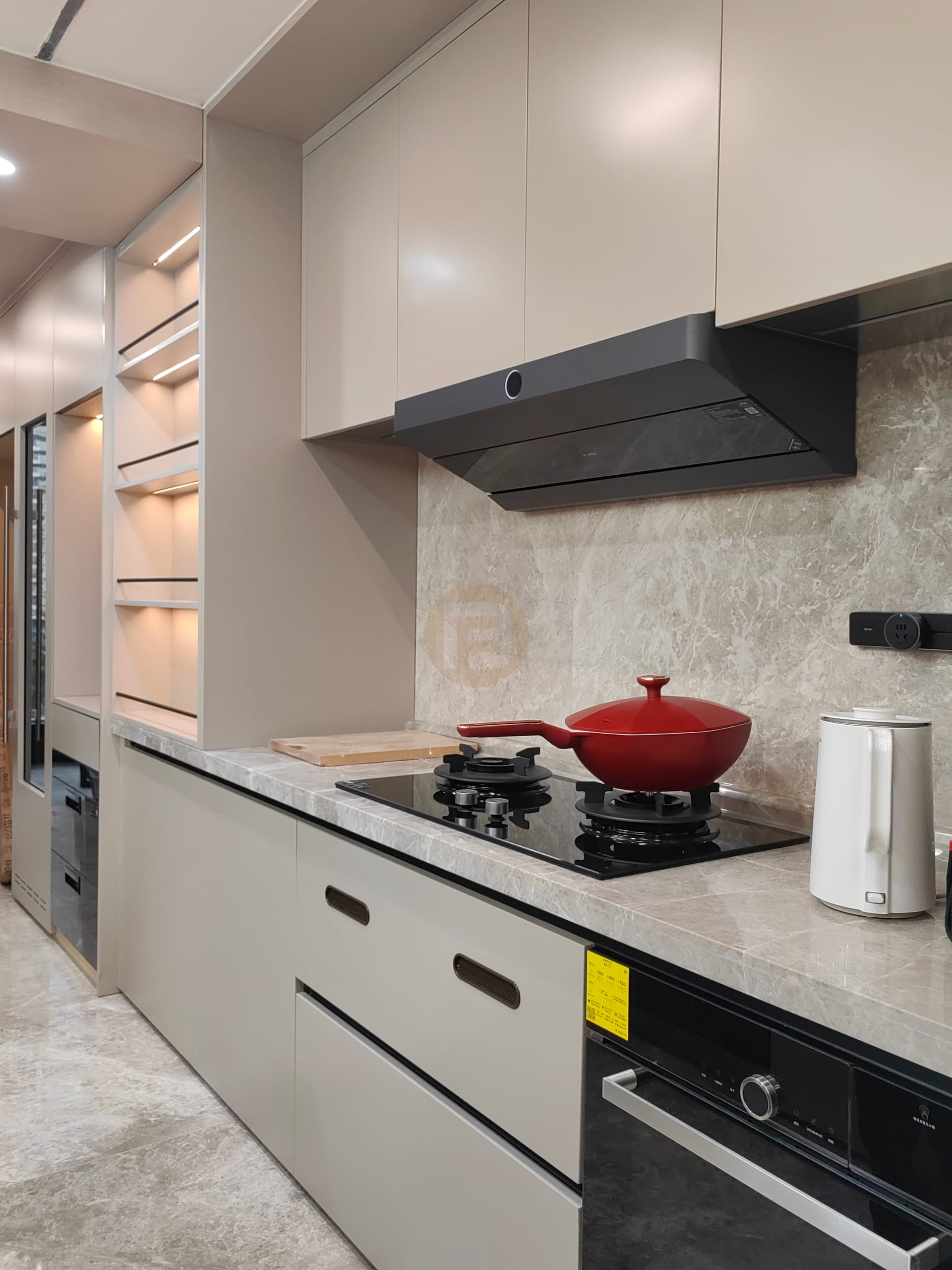 Beige stainless steel kitchen with slimline hood, marble splashback and red wok on the black hob