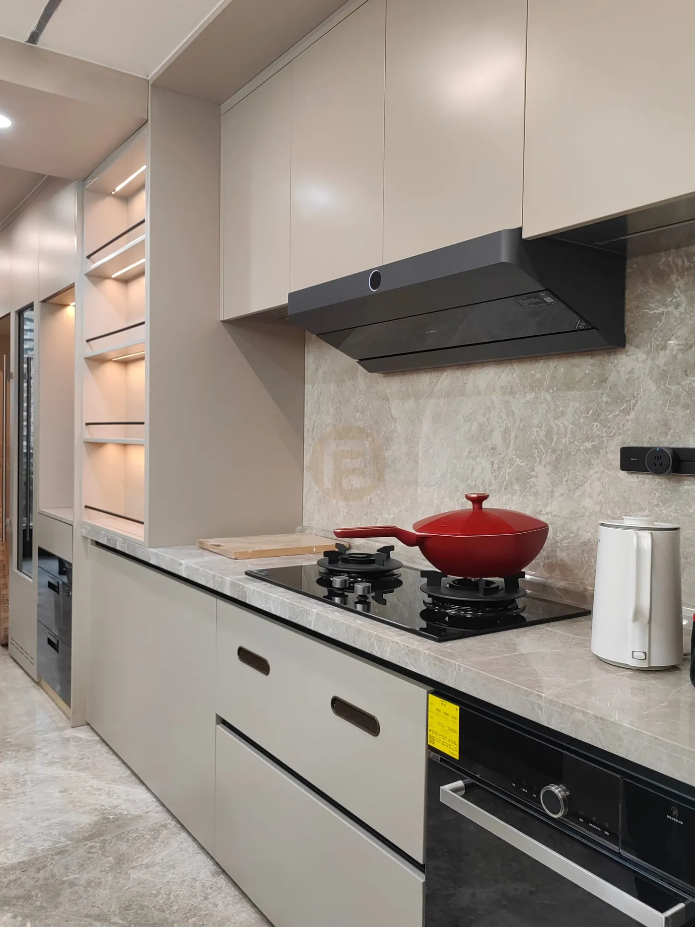 Beige stainless steel kitchen with slimline hood, marble splashback and red wok on the black hob