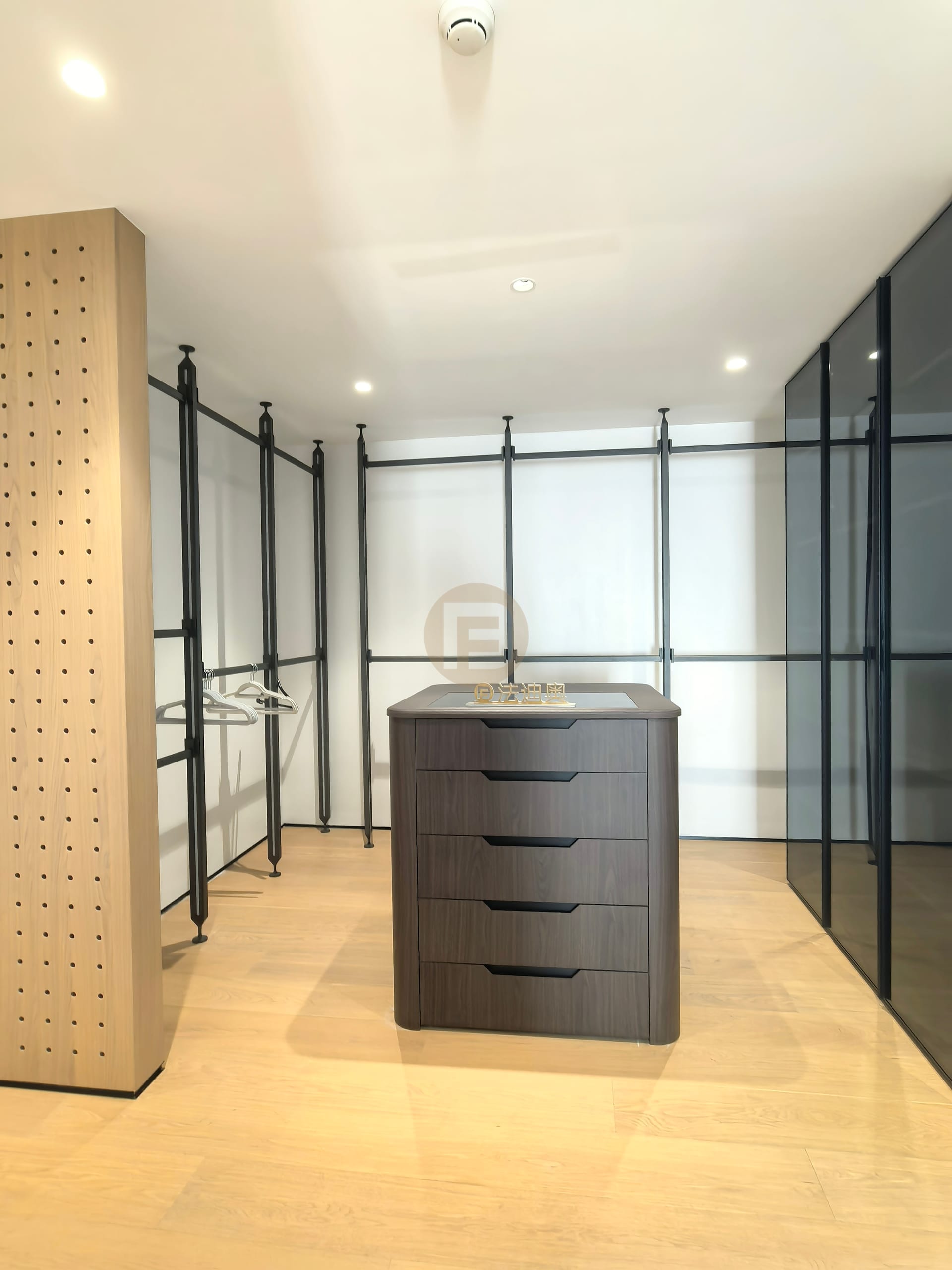 Walk-in closet with black steel hanging frames, smoked-glass panels and a central island of drawers