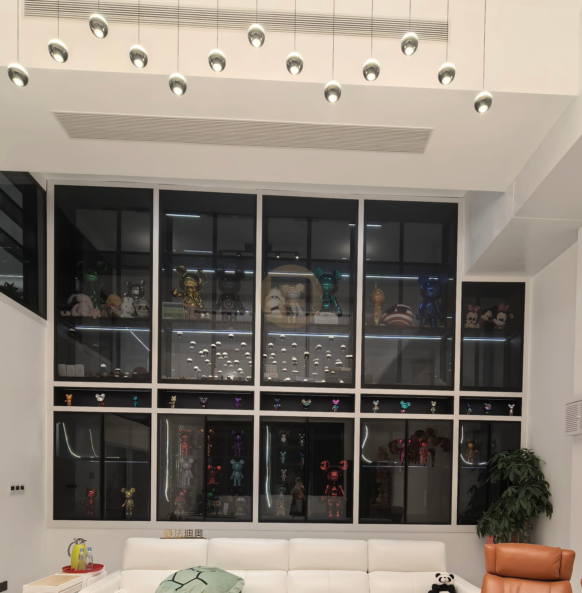 Double-height living room wall of black-framed glass display cabinets above a white sofa