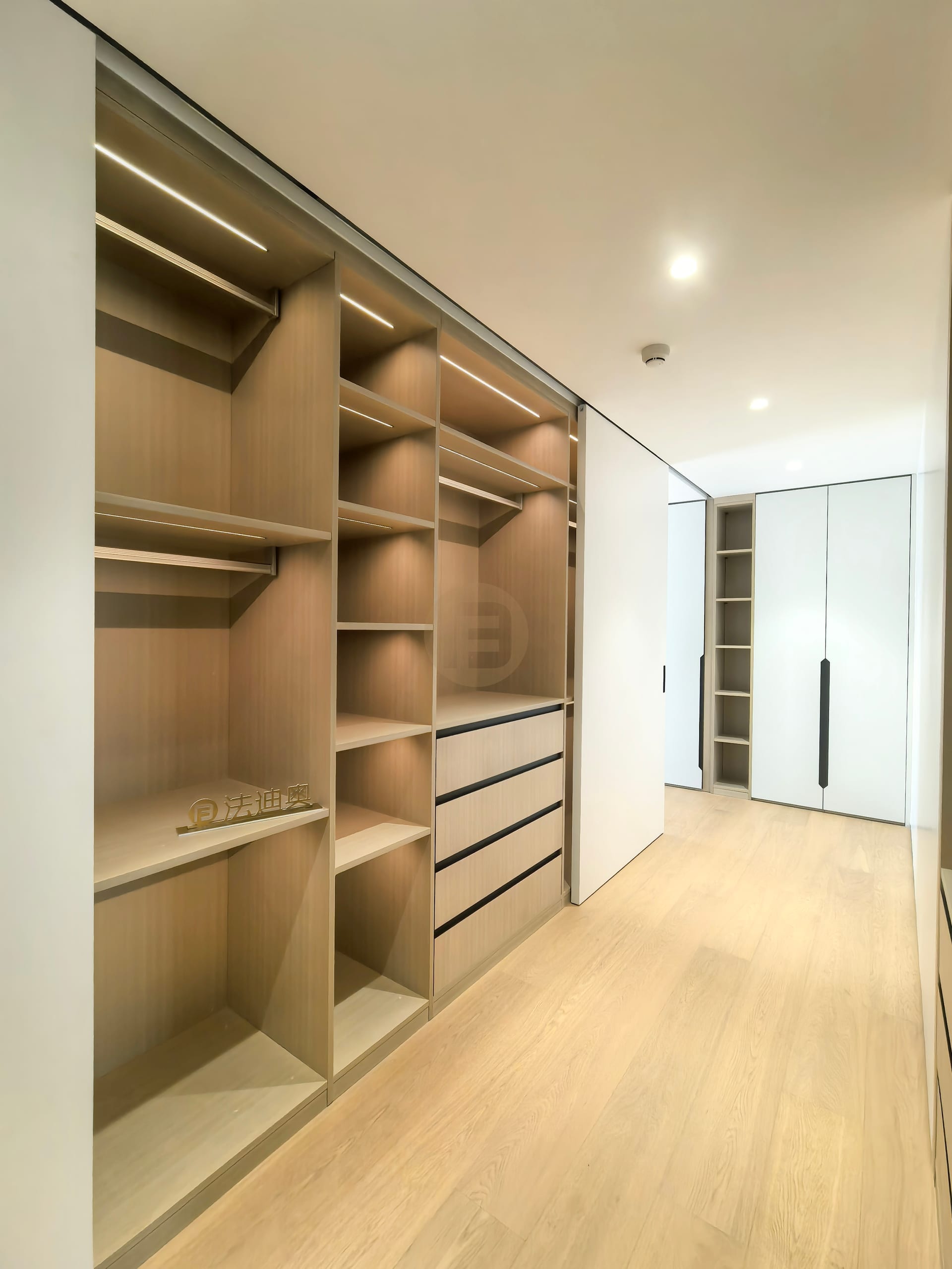 Open oak wardrobe run with lit rails, shelving and drawers sliding behind full-height white panels