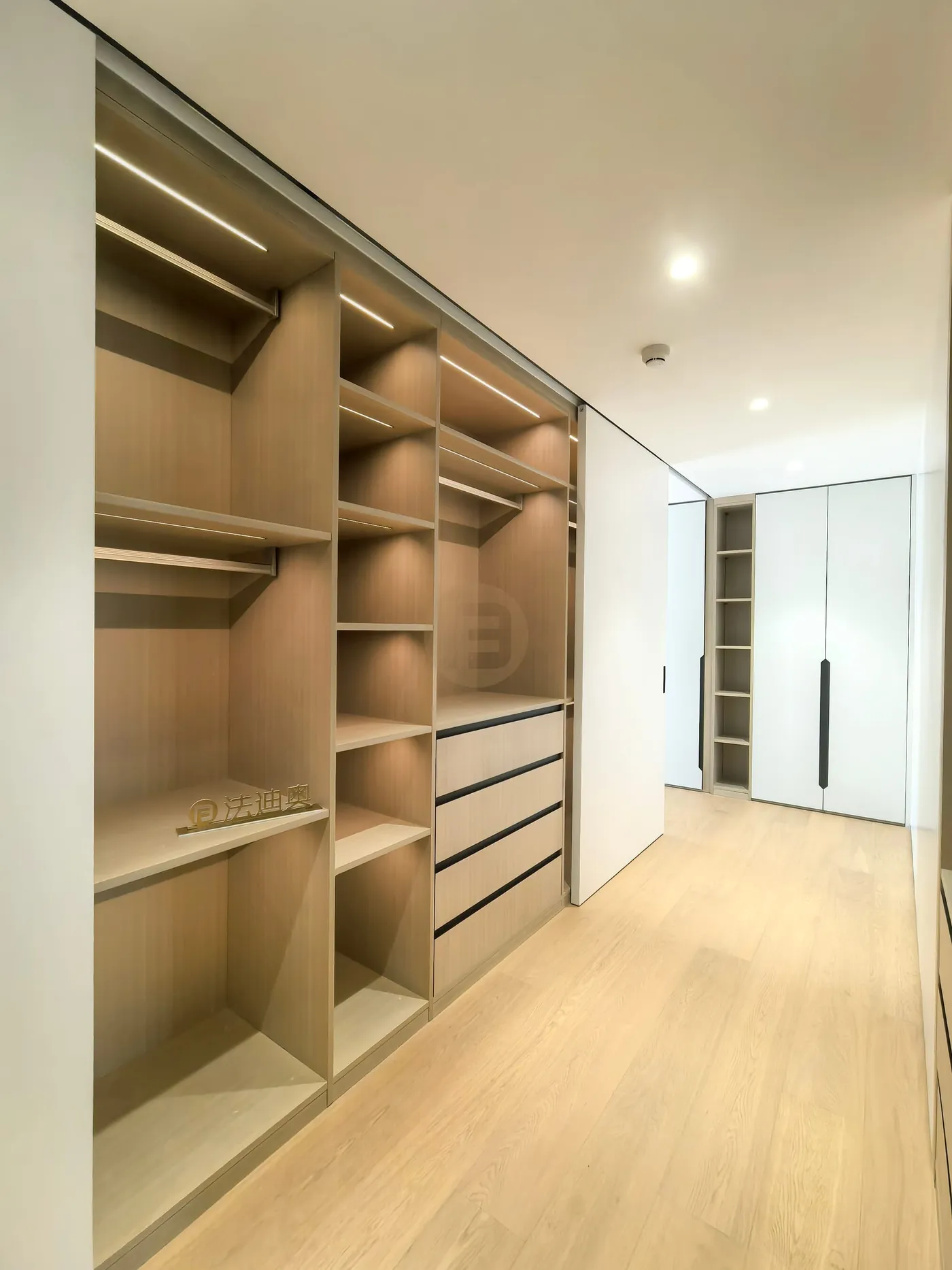 Open oak wardrobe run with lit rails, shelving and drawers sliding behind full-height white panels