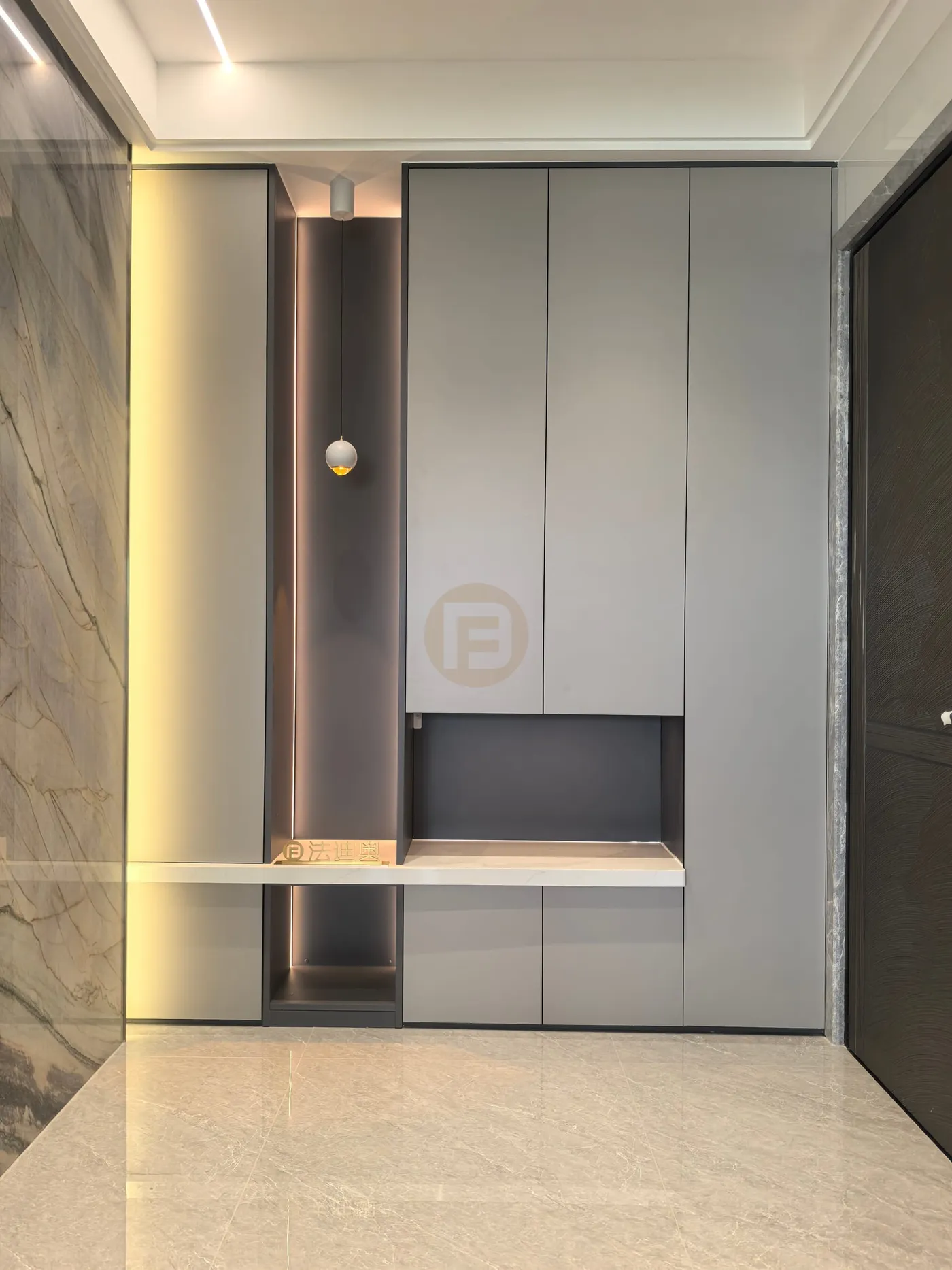 Entry console in grey stainless steel with illuminated niche, pendant light and marble-clad wall