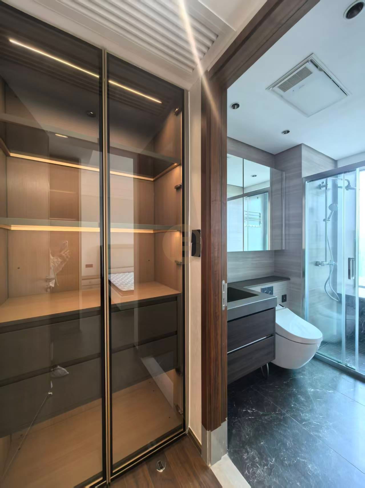 Glass-front linen cabinet beside a bathroom with dark wood-grain vanity, mirror wall and walk-in shower