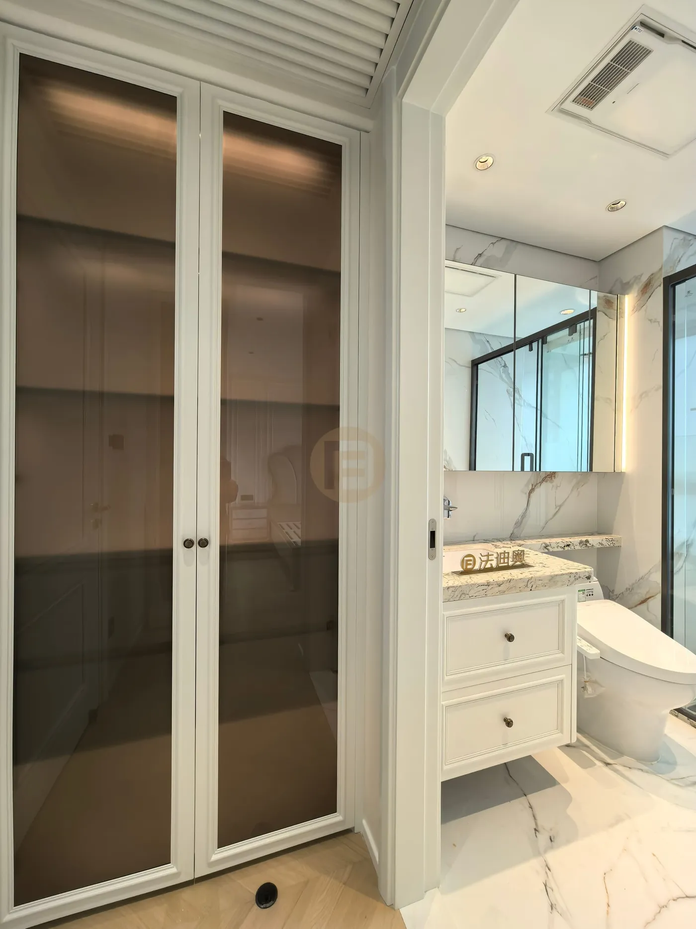 Bronze glass linen cabinet framing a marble bathroom with white stainless steel drawer vanity
