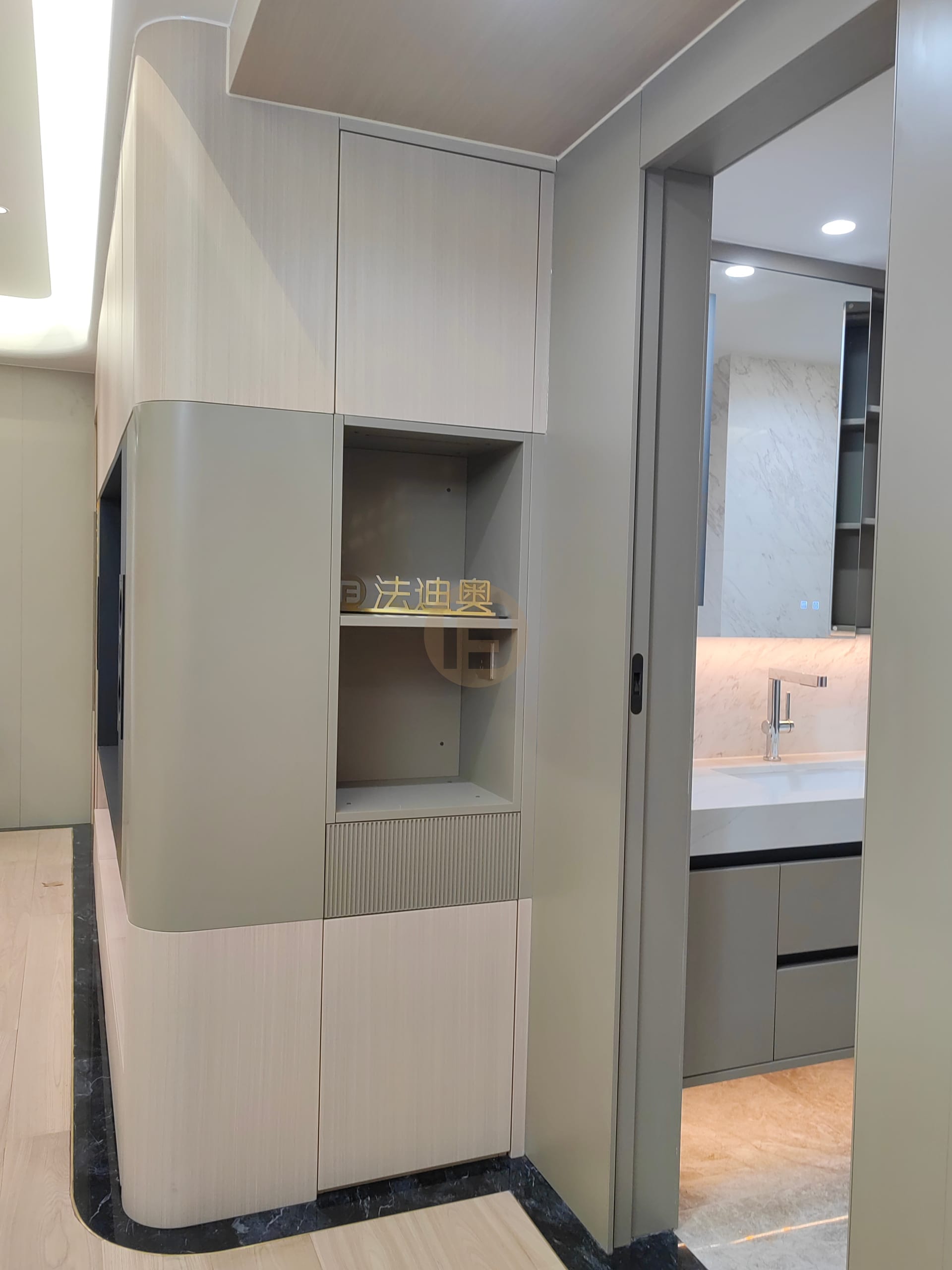 Curved hallway cabinet with display niche beside a pocket door opening to the vanity room