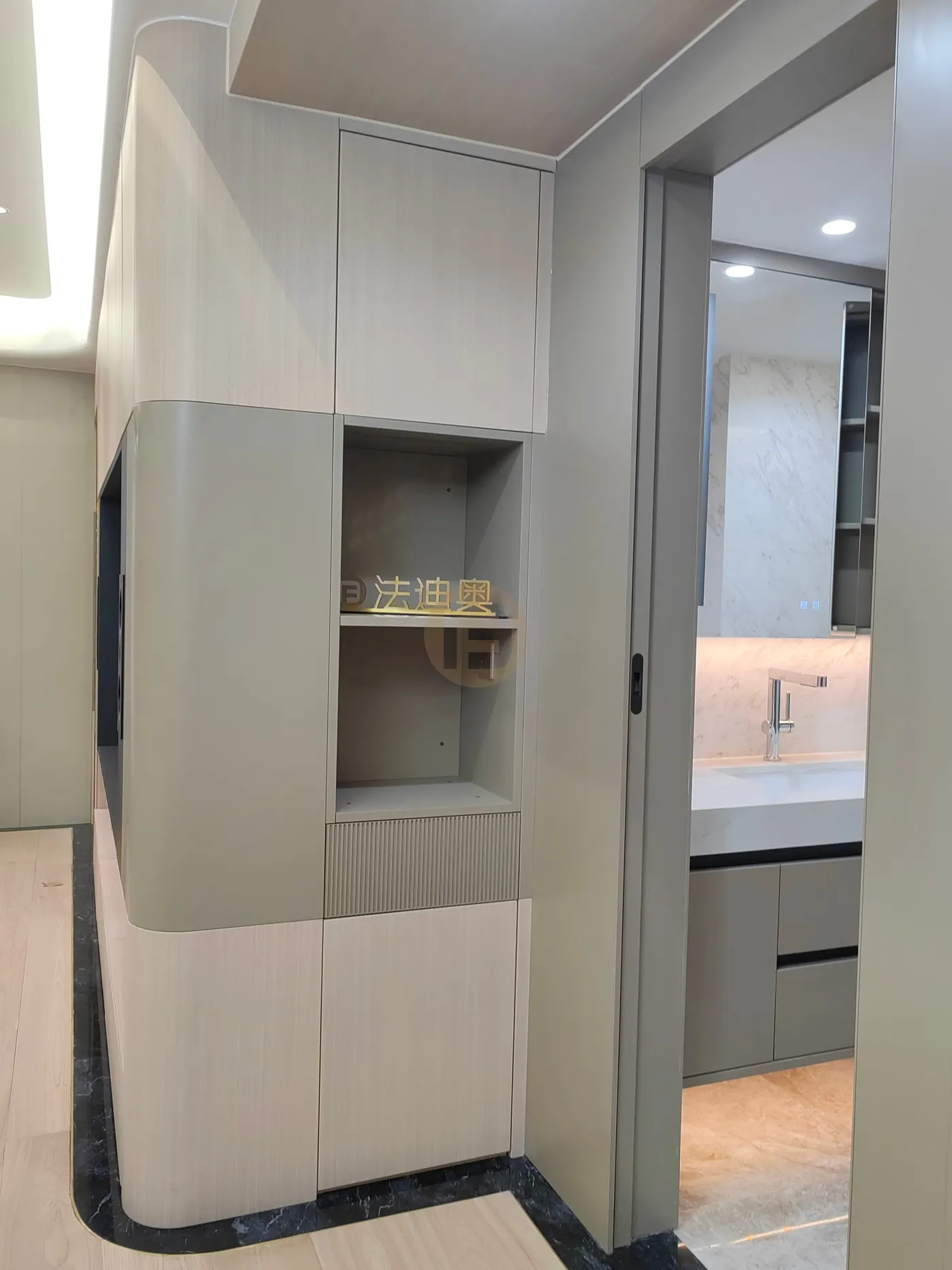 Curved hallway cabinet with display niche beside a pocket door opening to the vanity room