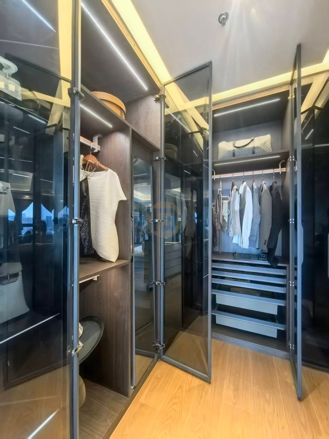 Smoked-glass wardrobe doors open to lit rails and metal-framed drawer stacks in the walk-in closet