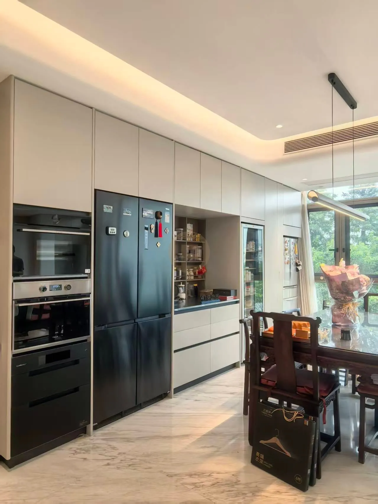 Open-plan kitchen with greige stainless steel cabinets, black appliance tower and rosewood dining chairs