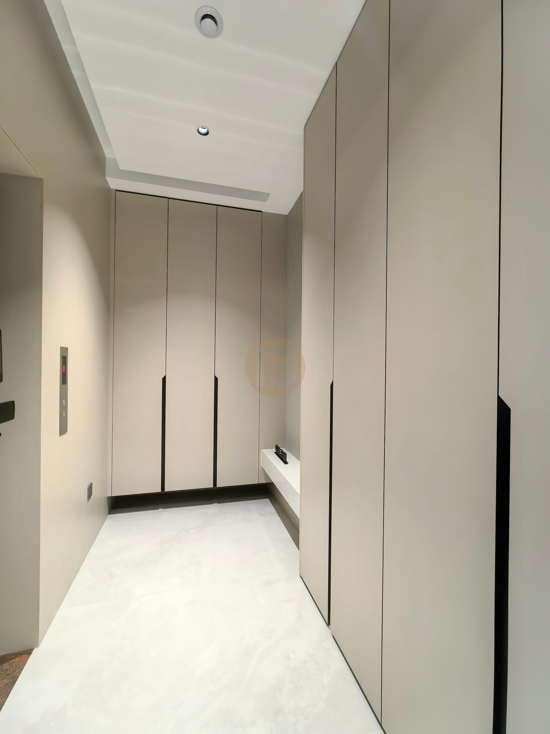 Entry hall lined with full-height champagne stainless steel wardrobes and a recessed bench niche