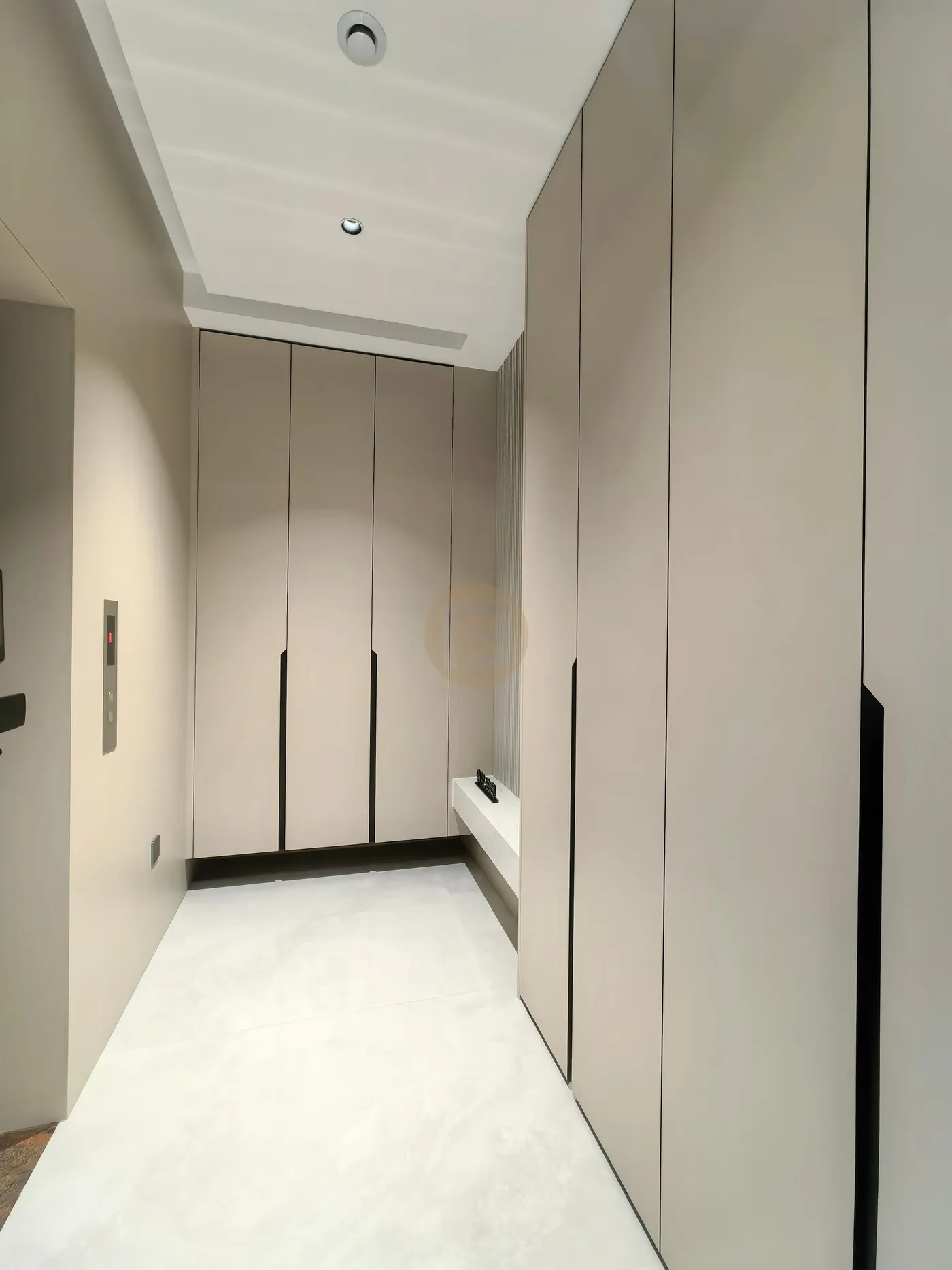 Entry hall lined with full-height champagne stainless steel wardrobes and a recessed bench niche