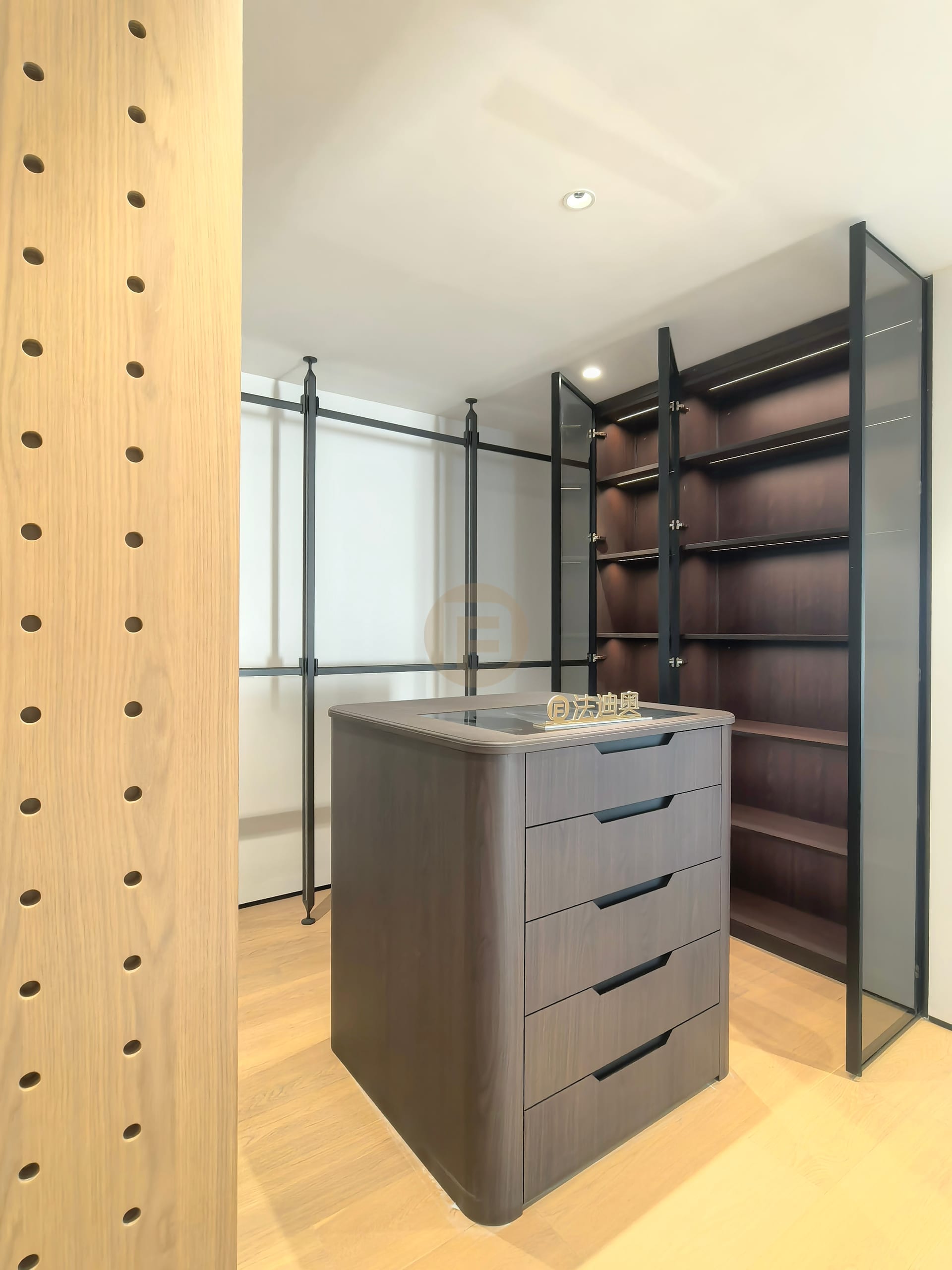 Dark timber display shelving behind smoked glass with a rounded stainless steel drawer island