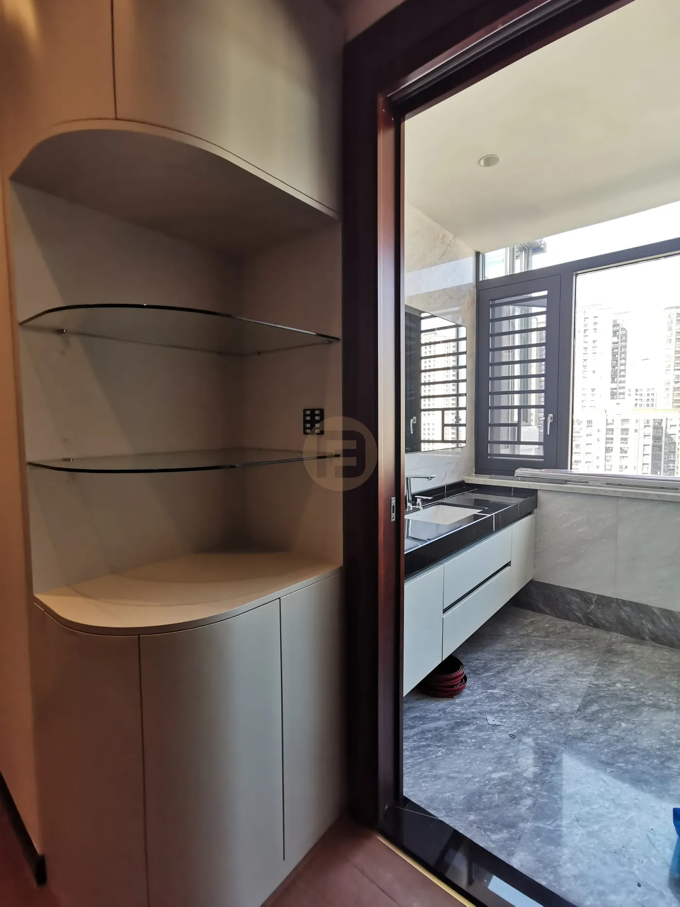 Curved-corner display shelving in taupe lacquer beside the doorway to the black stone vanity