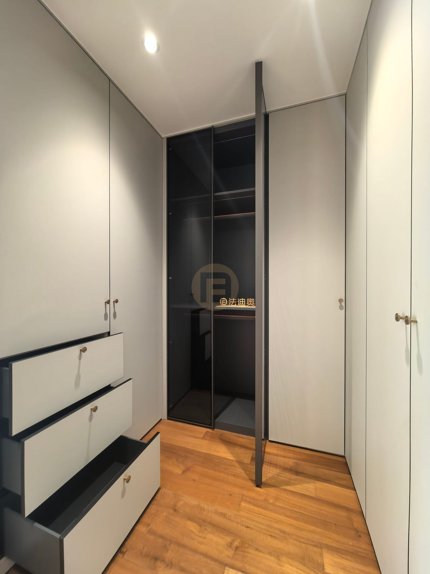 Grey lacquered wardrobes with brass knobs and stepped-open drawers beside a smoked-glass cabinet