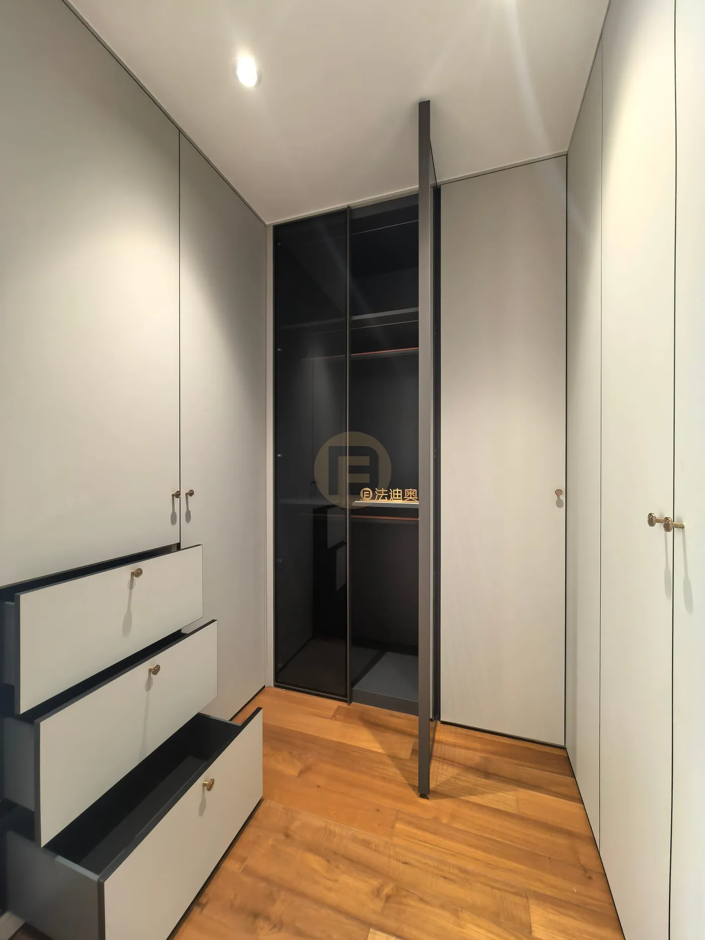 Grey lacquered wardrobes with brass knobs and stepped-open drawers beside a smoked-glass cabinet