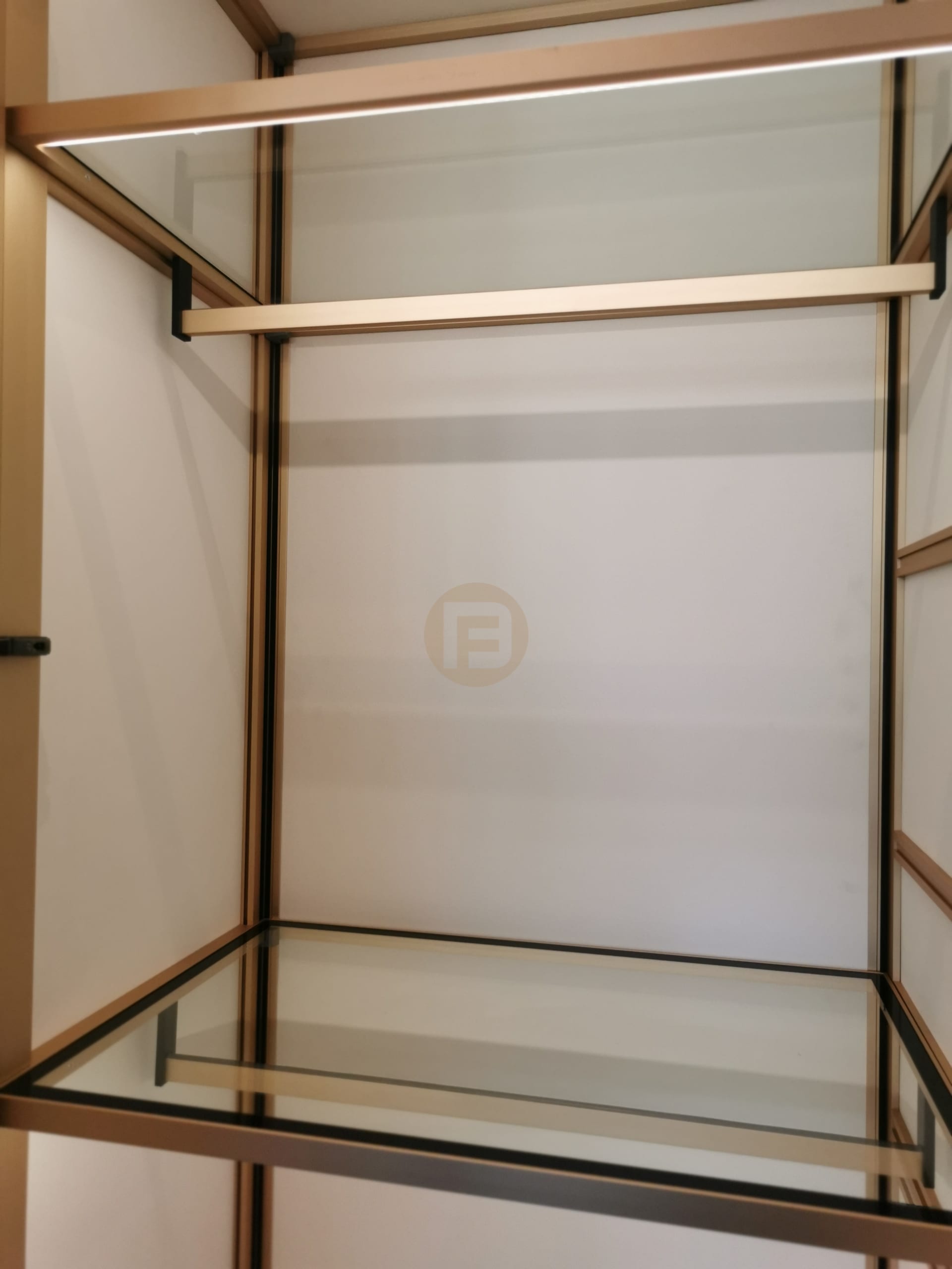 Detail of champagne-gold stainless steel wardrobe framing with glass shelves and integrated LED strip