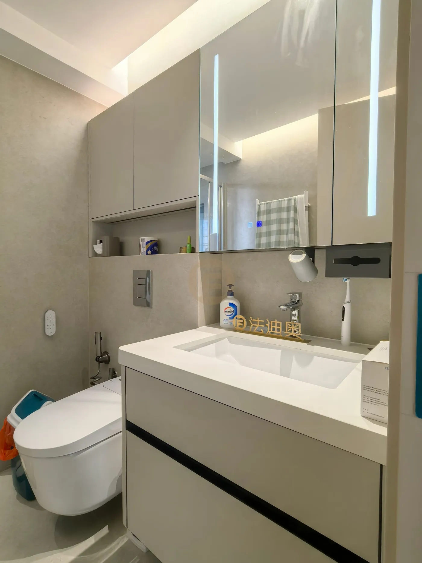 Greige bathroom vanity with stainless steel cabinetry, lit mirror cabinet and wall-hung storage