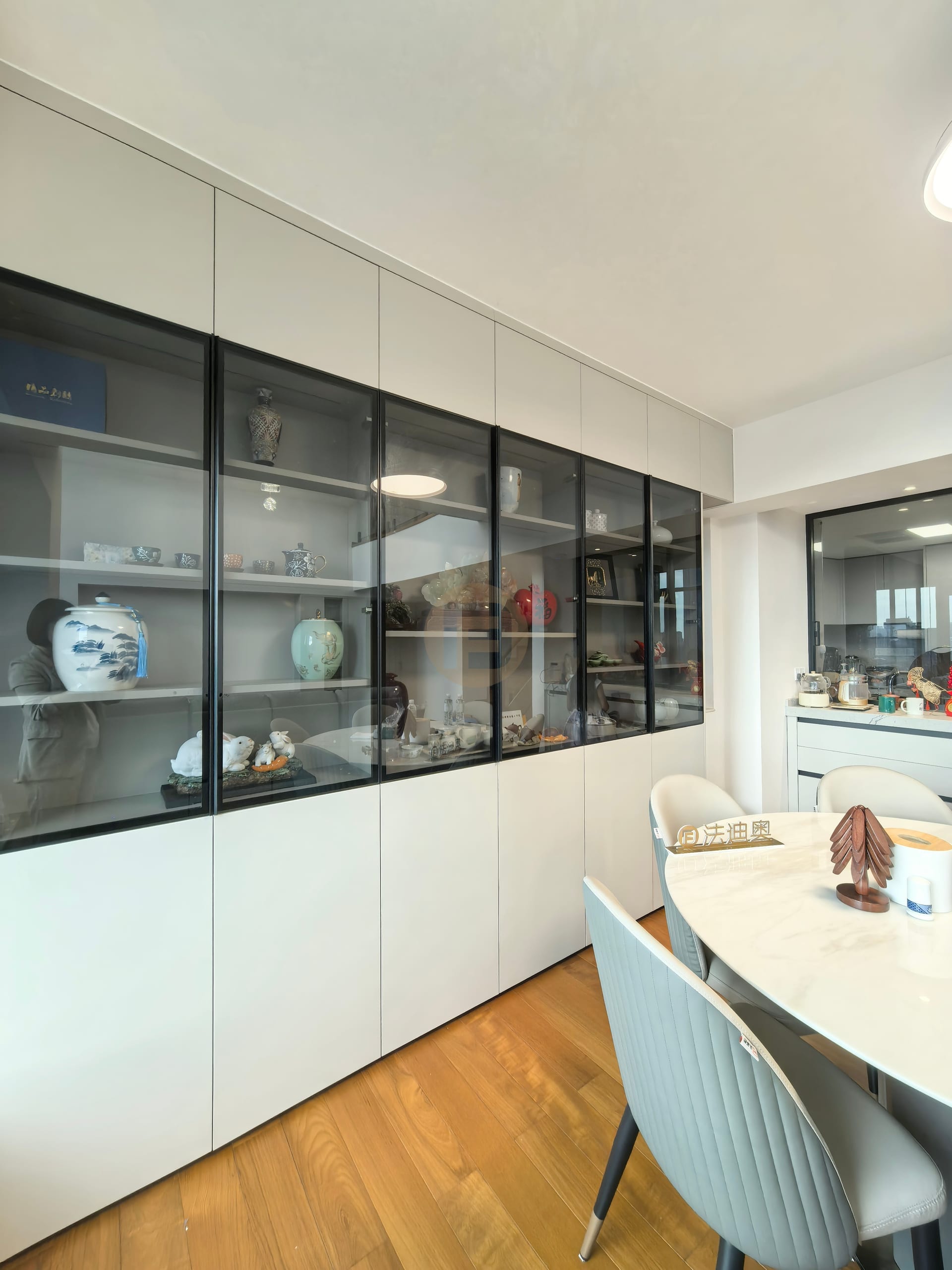 Glass-fronted dining room display wall in greige stainless steel cabinetry with black-framed doors