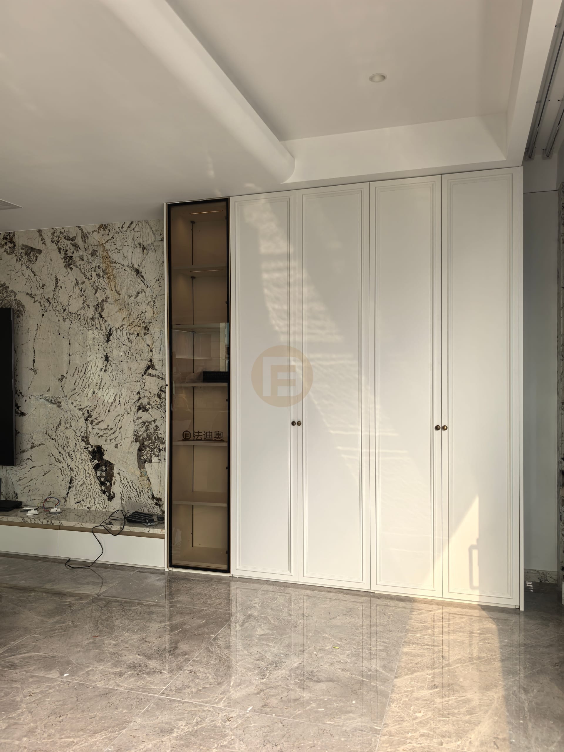 Living room with bookmatched marble media wall, white paneled wardrobe doors and bronze glass display column