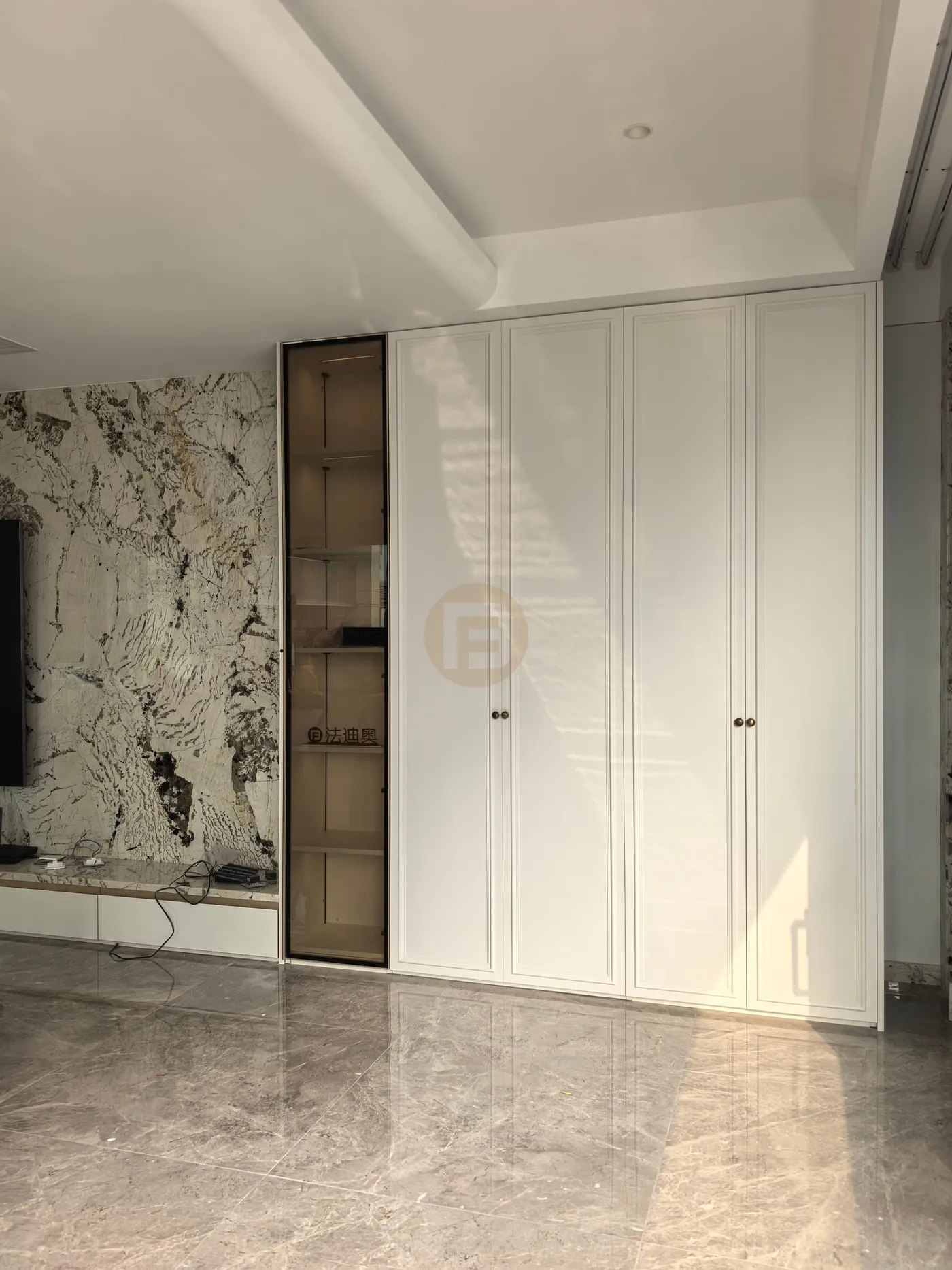 Living room with bookmatched marble media wall, white paneled wardrobe doors and bronze glass display column