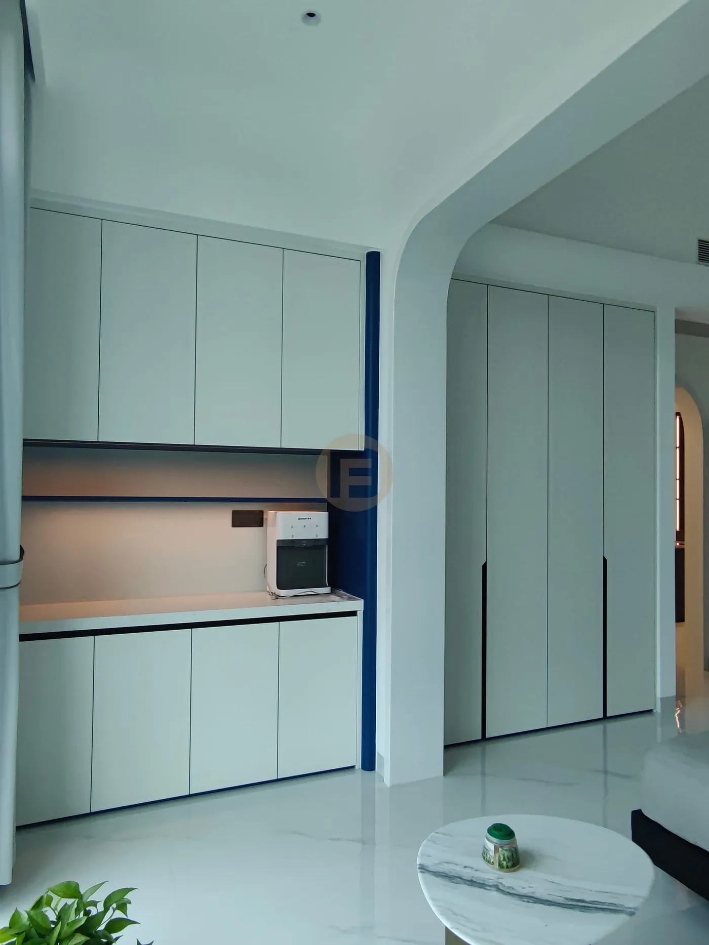 Pale sage sideboard cabinetry with a cobalt-lined niche beside an arched opening