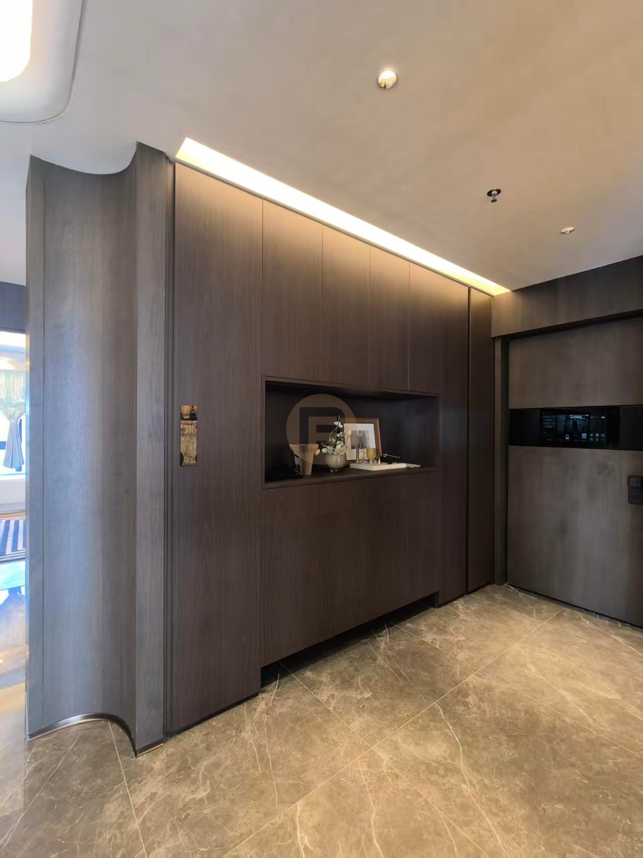 Curved full-height dark-wood stainless steel cabinetry wall with a lit display niche near the entry