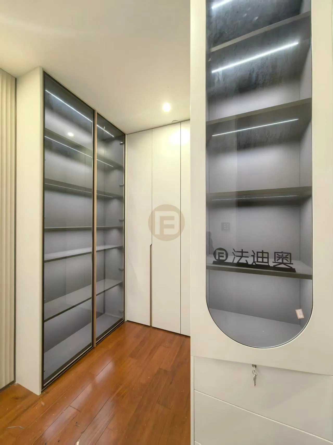 Smoked-glass sliding wardrobes and a curved glass display tower in cream stainless steel