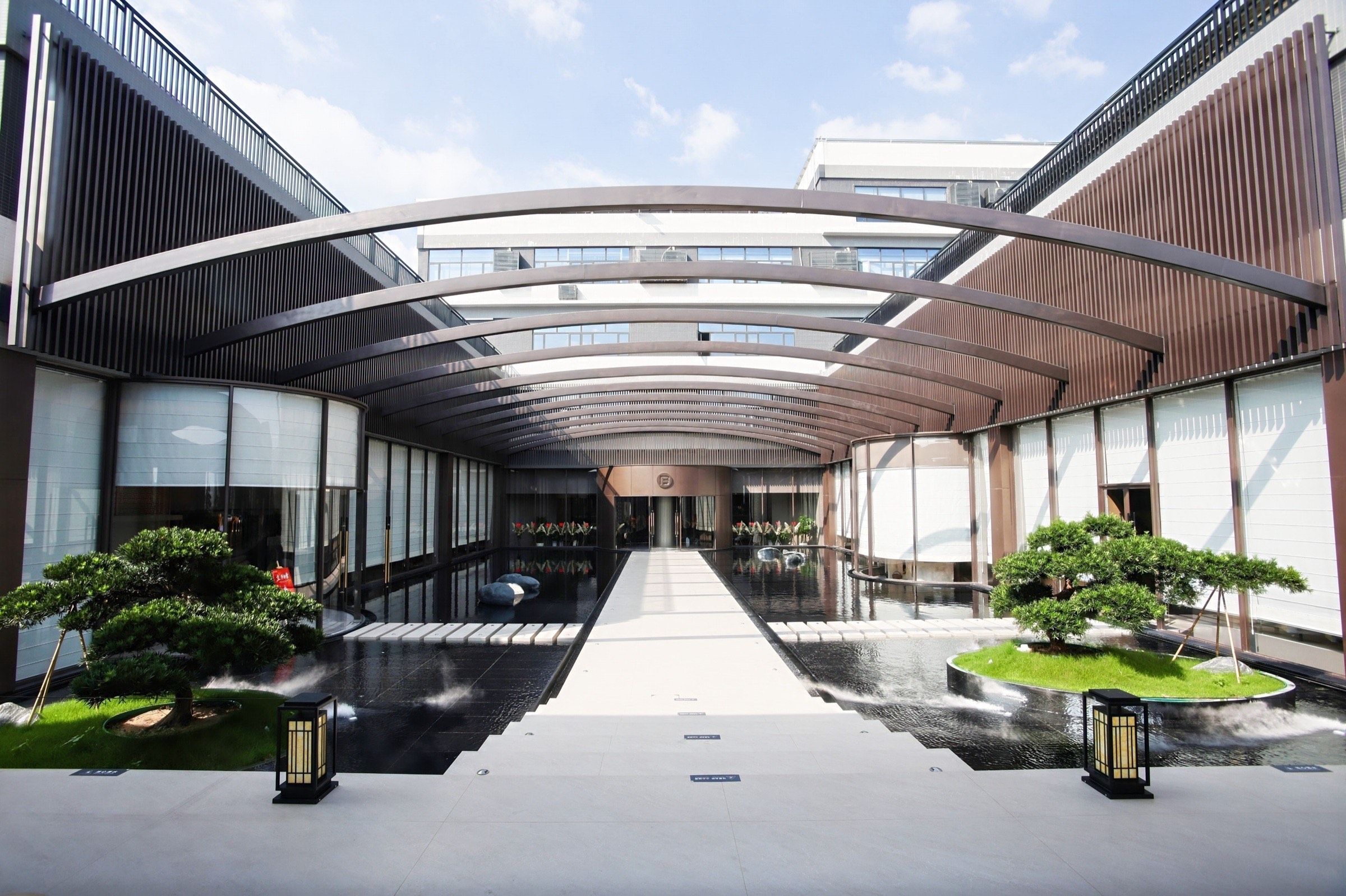 Open-air courtyard walkway at Fadior's Foshan showroom with a steel-and-glass canopy and landscaped islands.