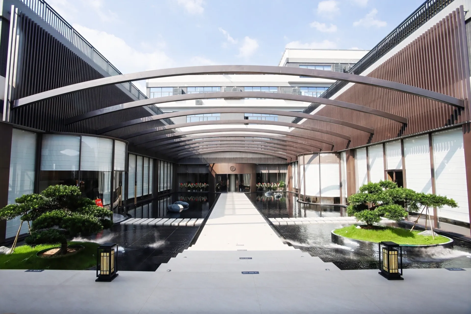Open-air courtyard walkway at Fadior's Foshan showroom with a steel-and-glass canopy and landscaped islands.