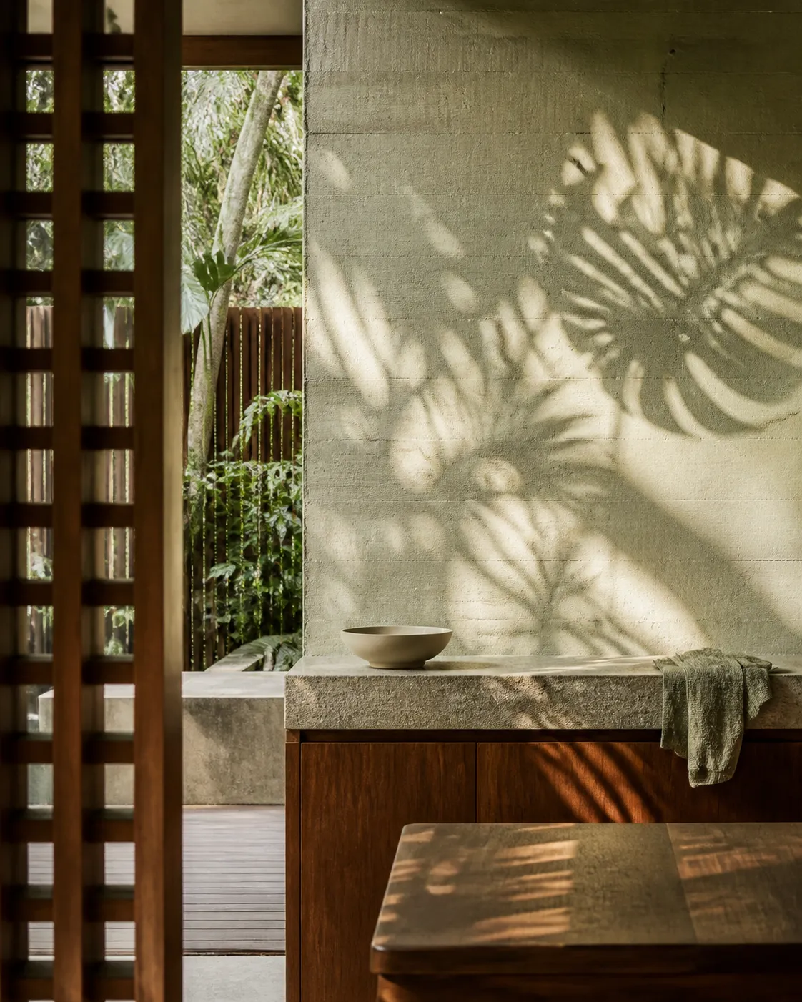 Concrete kitchen wall, timber counter, linen and leaf shadows in a tropical material mood study.