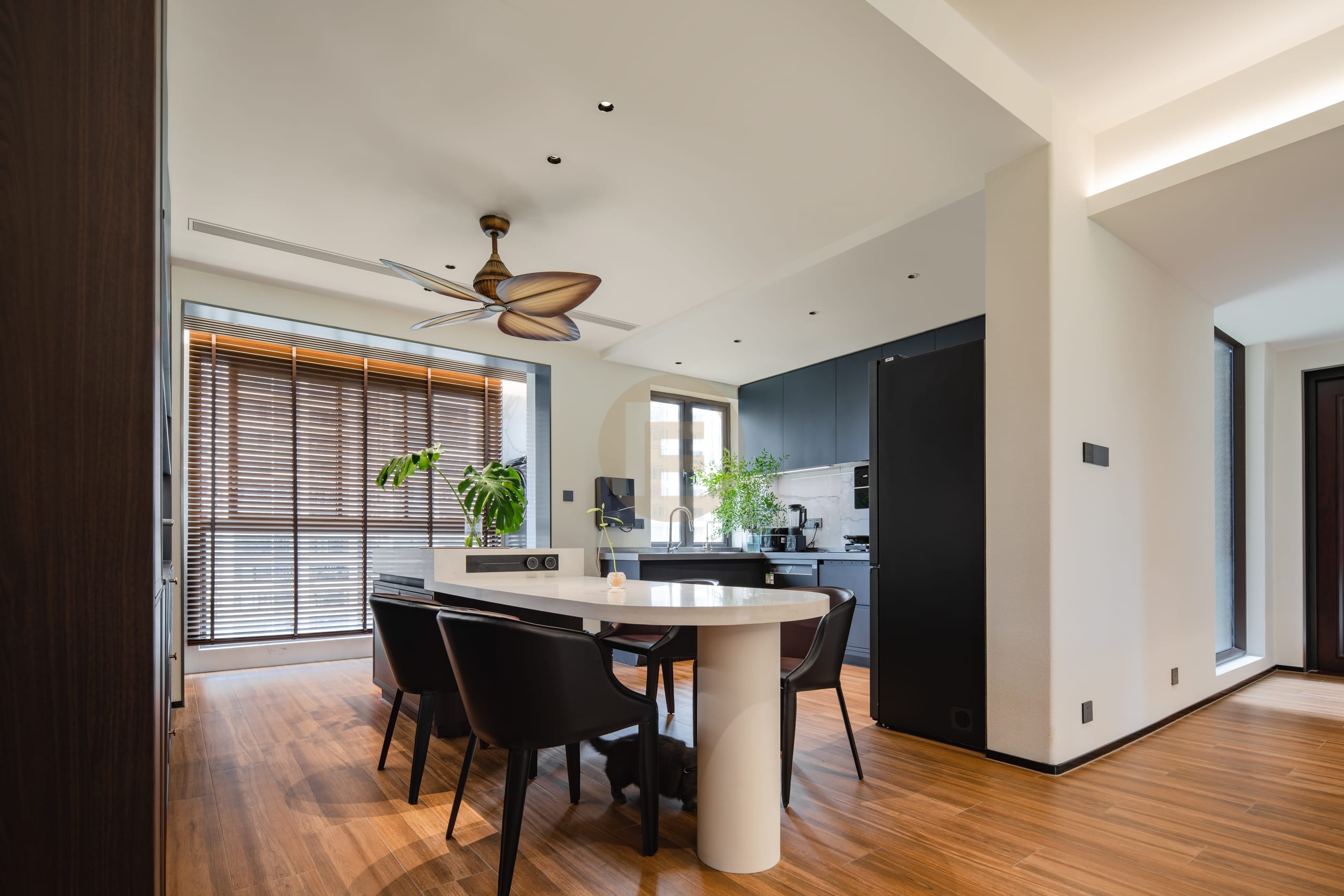 Walnut-floored dining area opening to a dark stainless steel kitchen with white worktop and ceiling fan