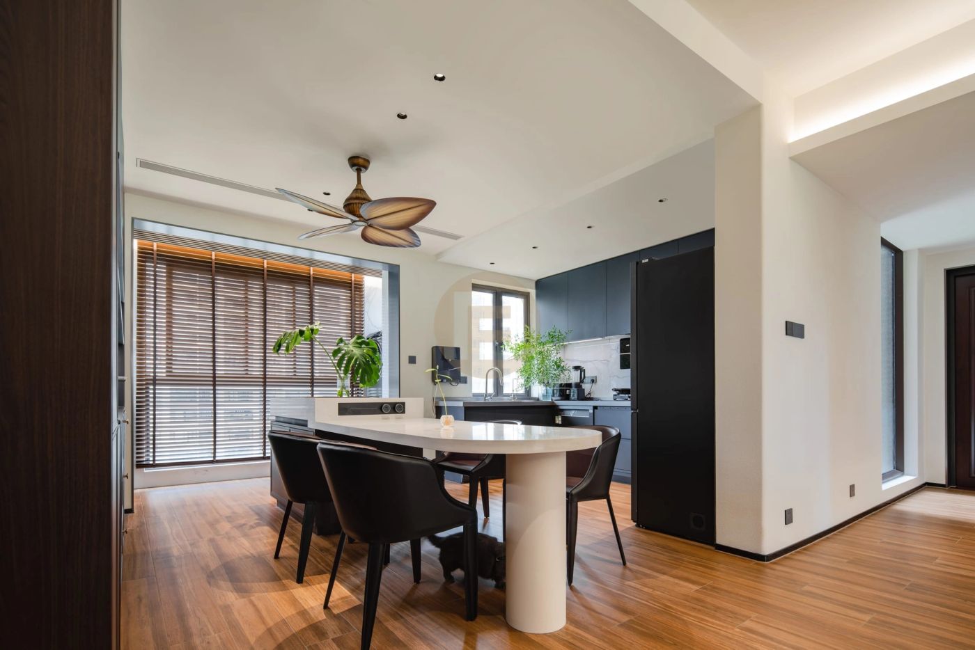 Walnut-floored dining area opening to a dark stainless steel kitchen with white worktop and ceiling fan