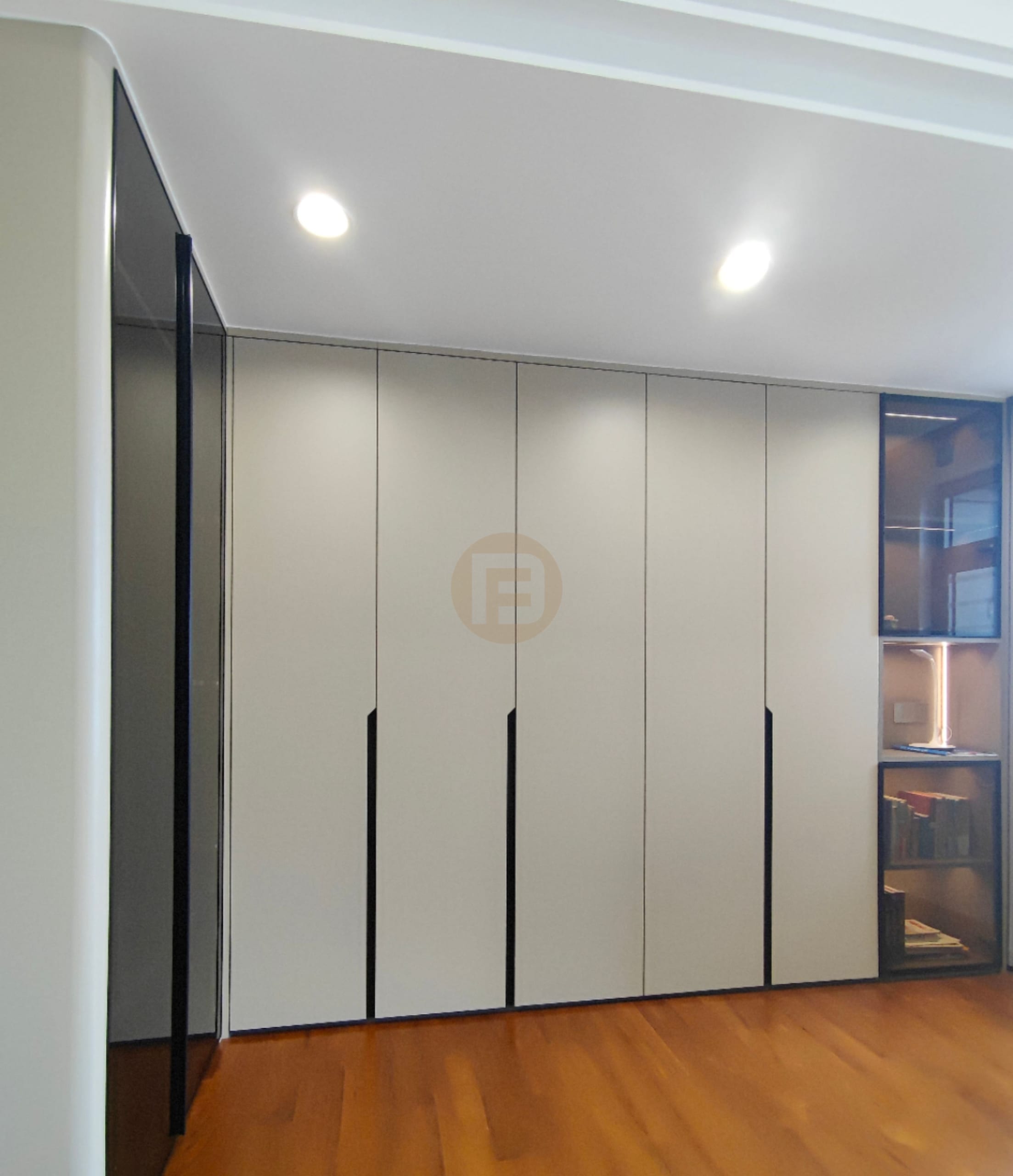 Warm beige stainless steel wardrobe wall with black recessed pulls beside a lit glass display cabinet