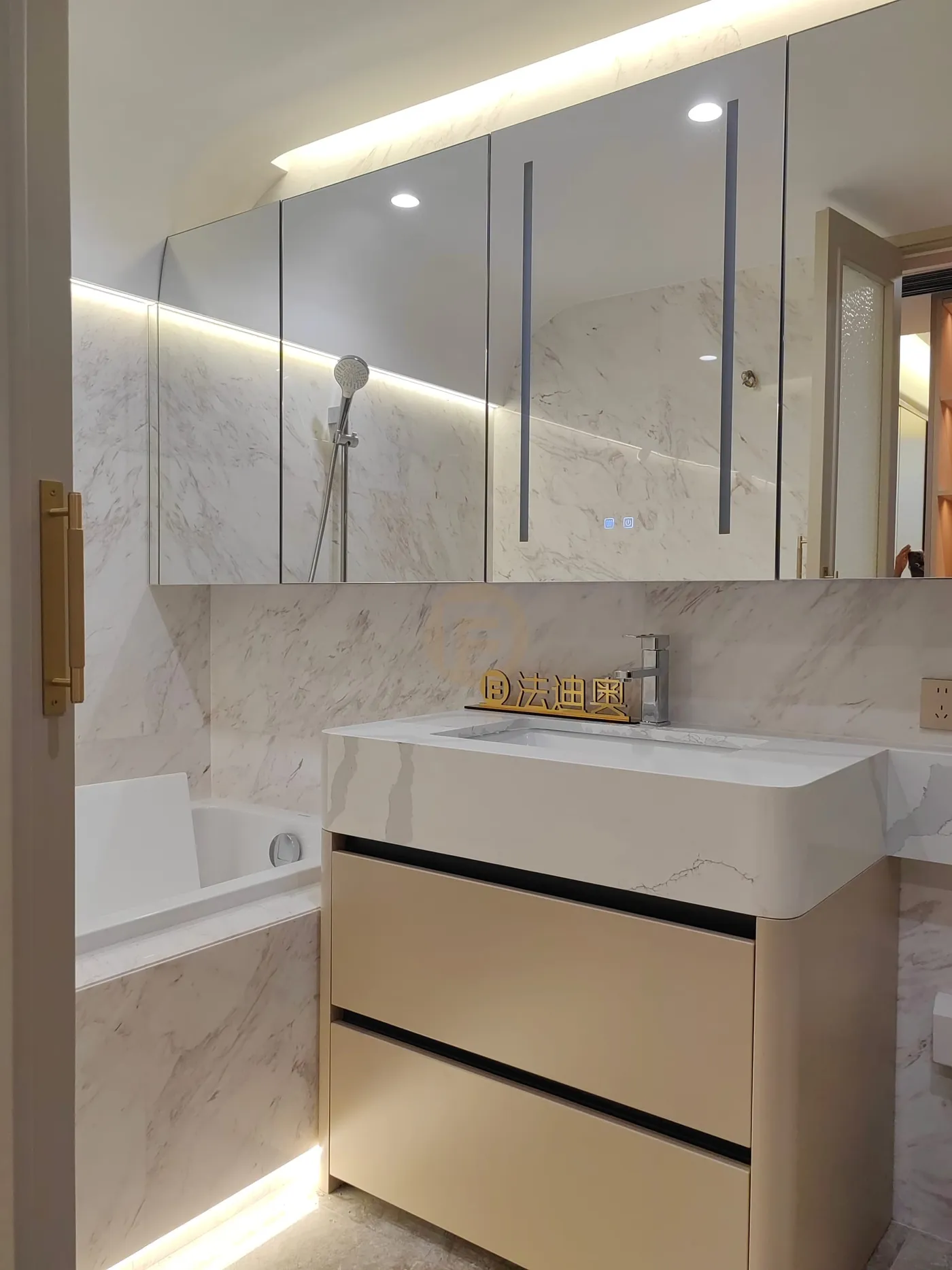 Cream stainless steel bathroom vanity with stone top, mirrored cabinet wall, brass pull and bathtub beyond