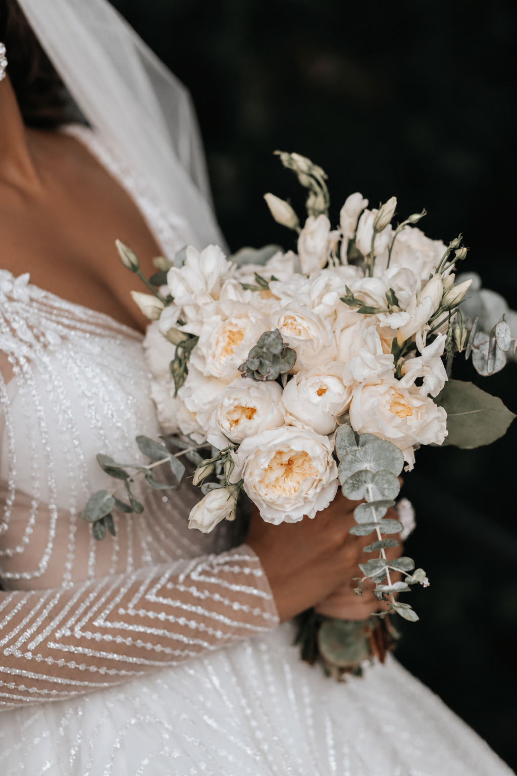 African bride holding an ivory and white bridal bouquet against a dark background.