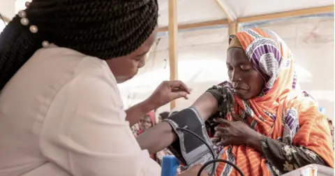 A health worker taking a woman's blood pressure at a field clinic