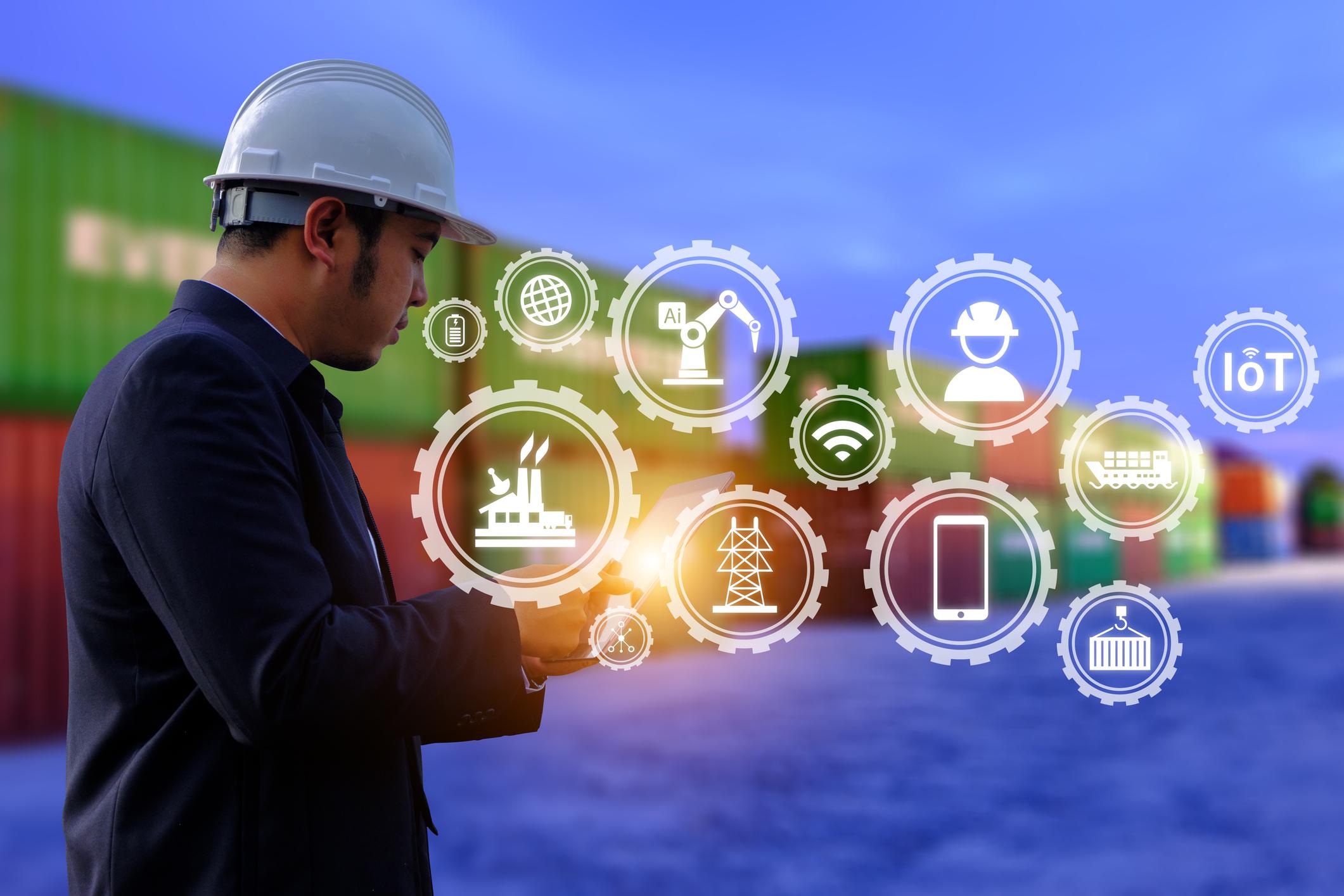 Logistics manager in a hard hat using a tablet at a shipping container port, with cellular IoT icons for connected supply chain assets