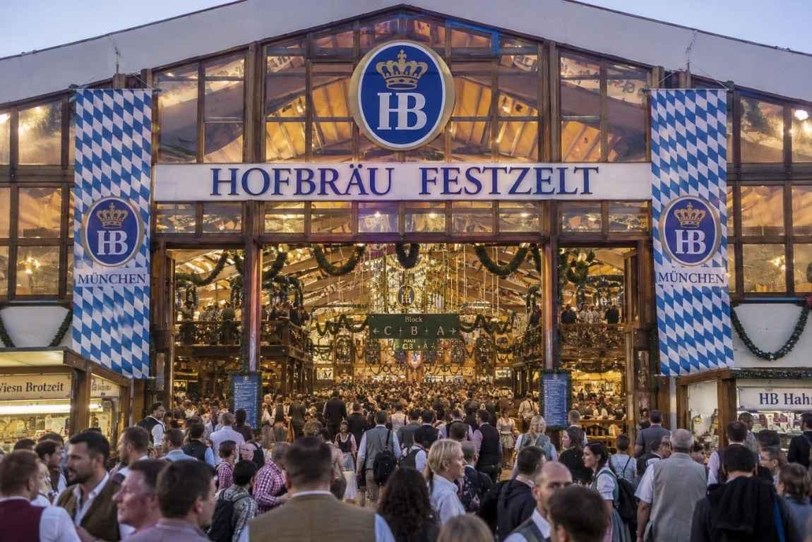 Crowds entering the Hofbräu Festzelt beer tent at Oktoberfest in Munich, decorated with blue-and-white Bavarian banners.