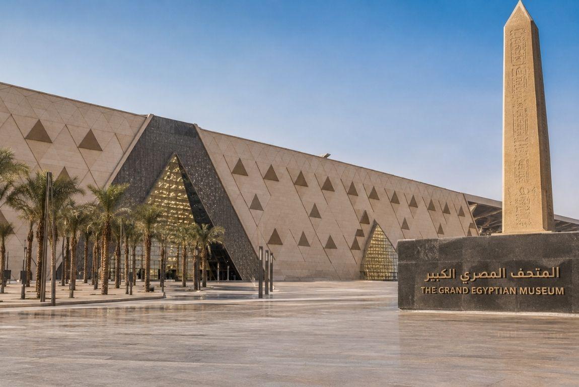 Exterior of the Grand Egyptian Museum in Giza, Egypt, featuring its modern geometric facade and a tall ancient-style obelisk.