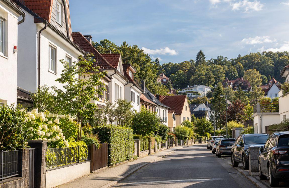 Quiet residential neighborhood in Germany with traditional homes, greenery, and parked cars.