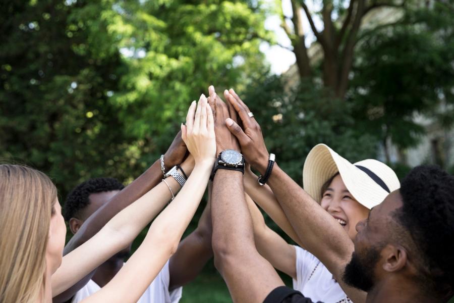 Smiling group of colleagues raising their hands together outdoors