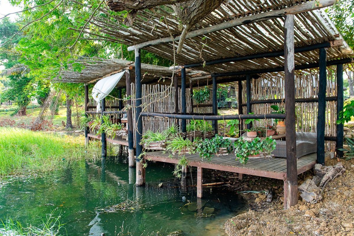 Covered wooden lounge deck built out over the water's edge, plants along the rail