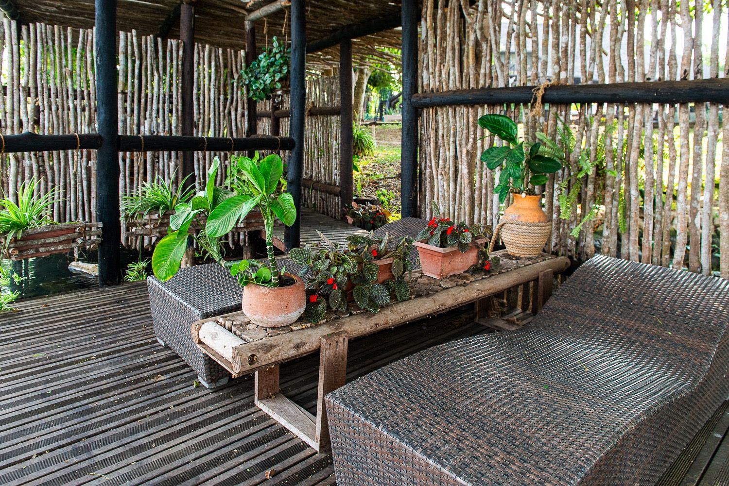 Shaded deck with wicker loungers and potted plants behind reed walls