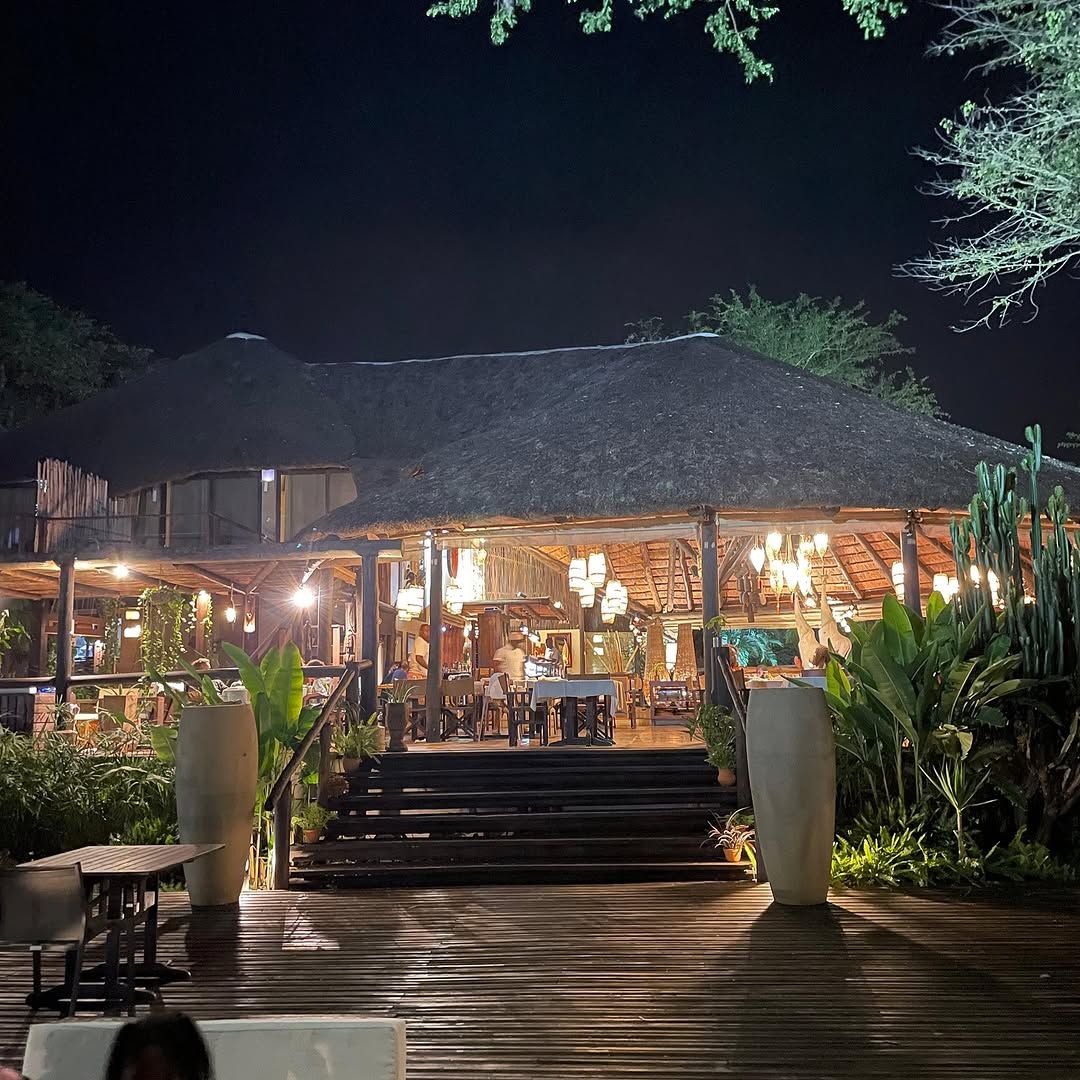 The thatched lakeside restaurant lit up at night, with steps up from the wooden deck