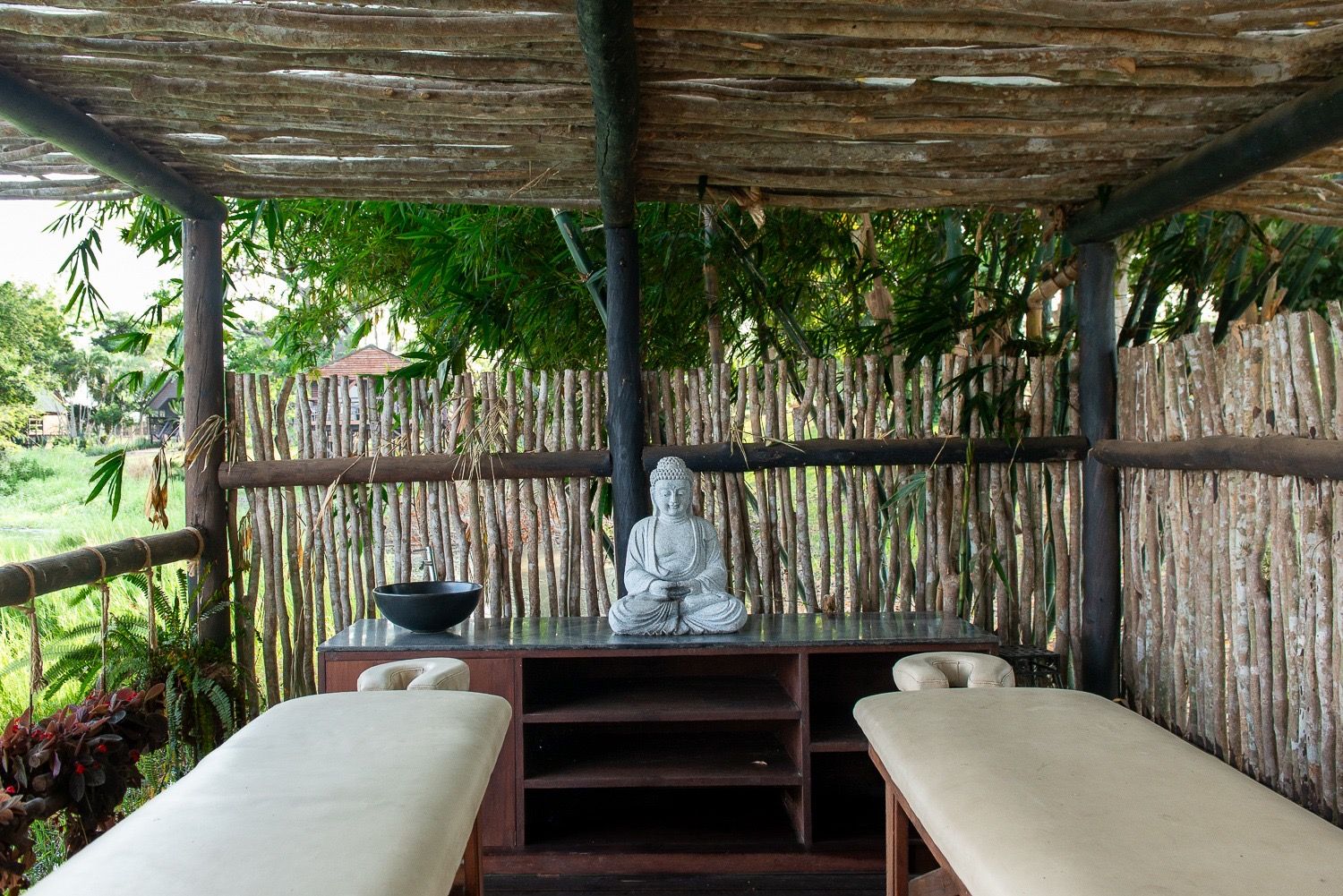 Two massage beds in an open-air pavilion with reed walls and a Buddha statue